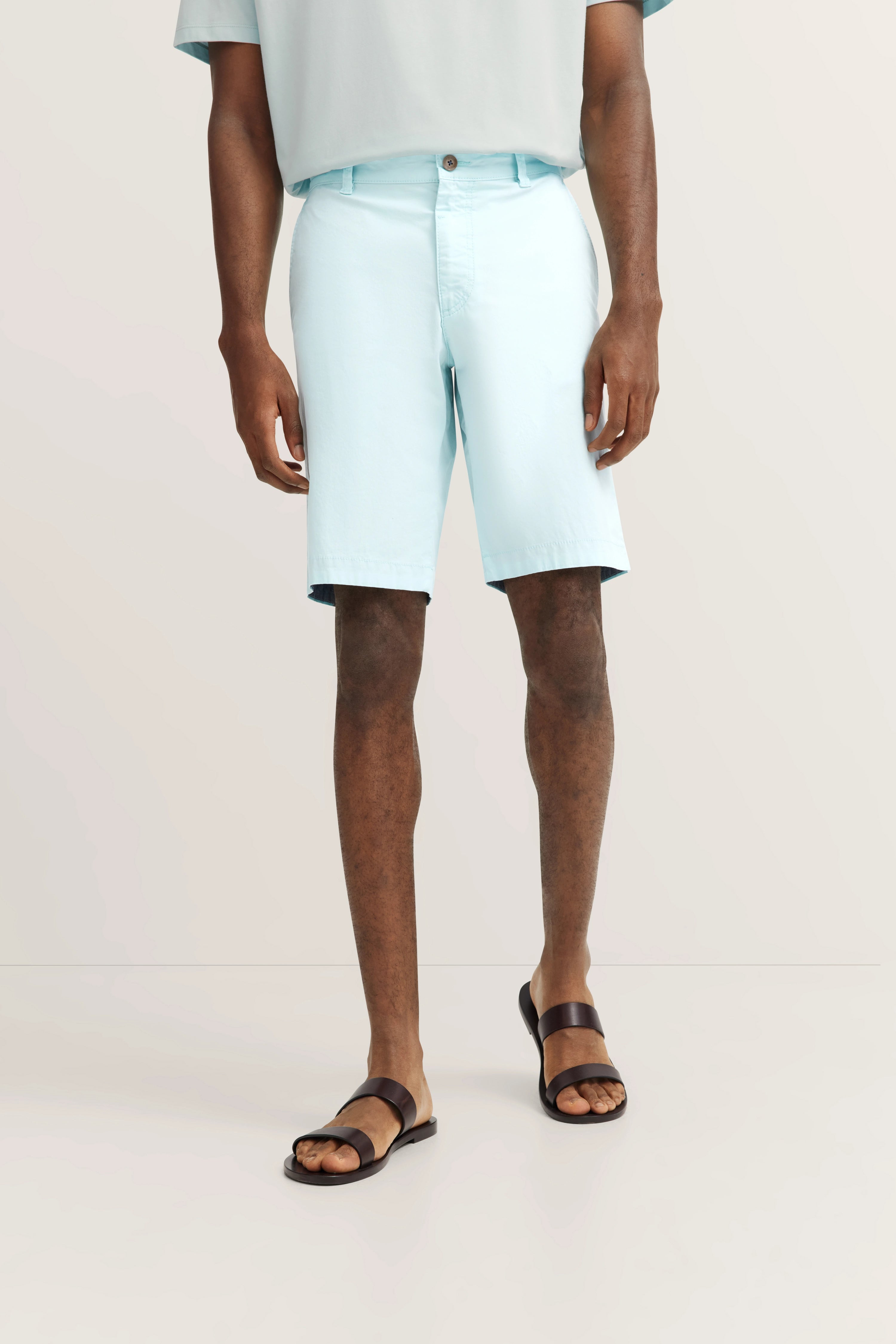 Hellblaue Shorts und Sandalen, legeres Modelbild, entspannter Stand.