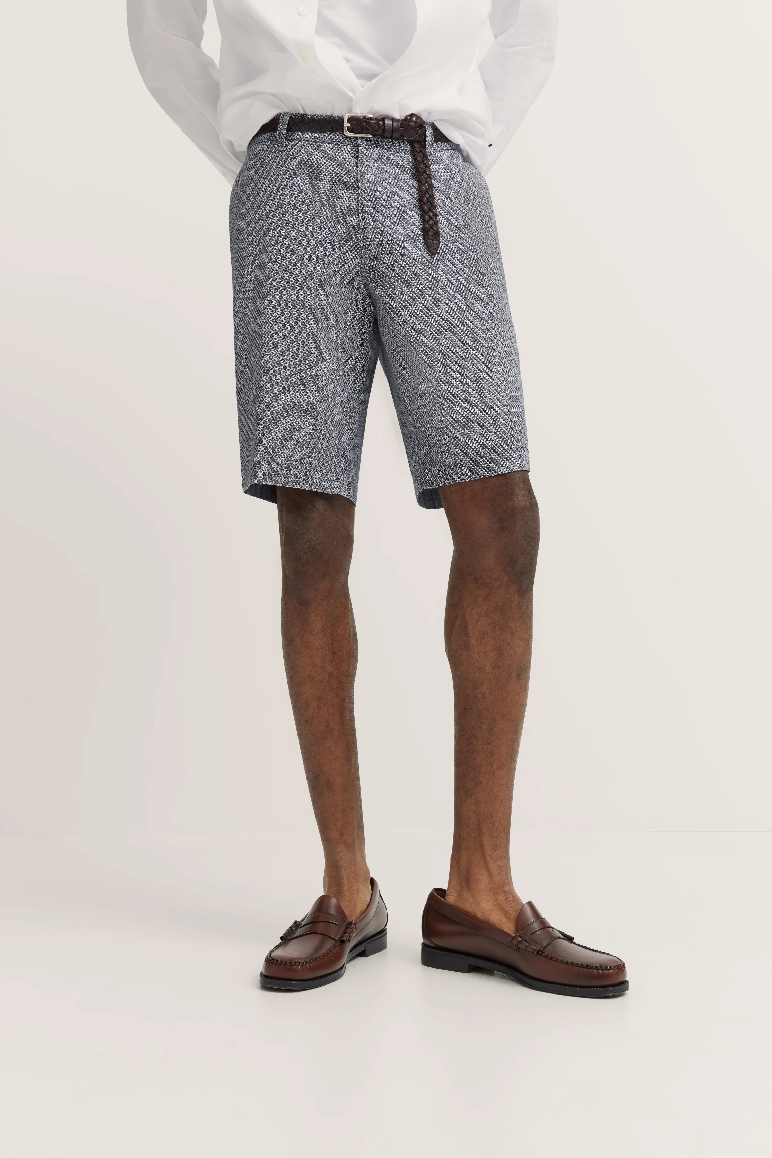 bugatti Outfit: weißes Hemd, graue gemusterte Shorts, braune Schuhe, legeres Modelbild ohne Posing.