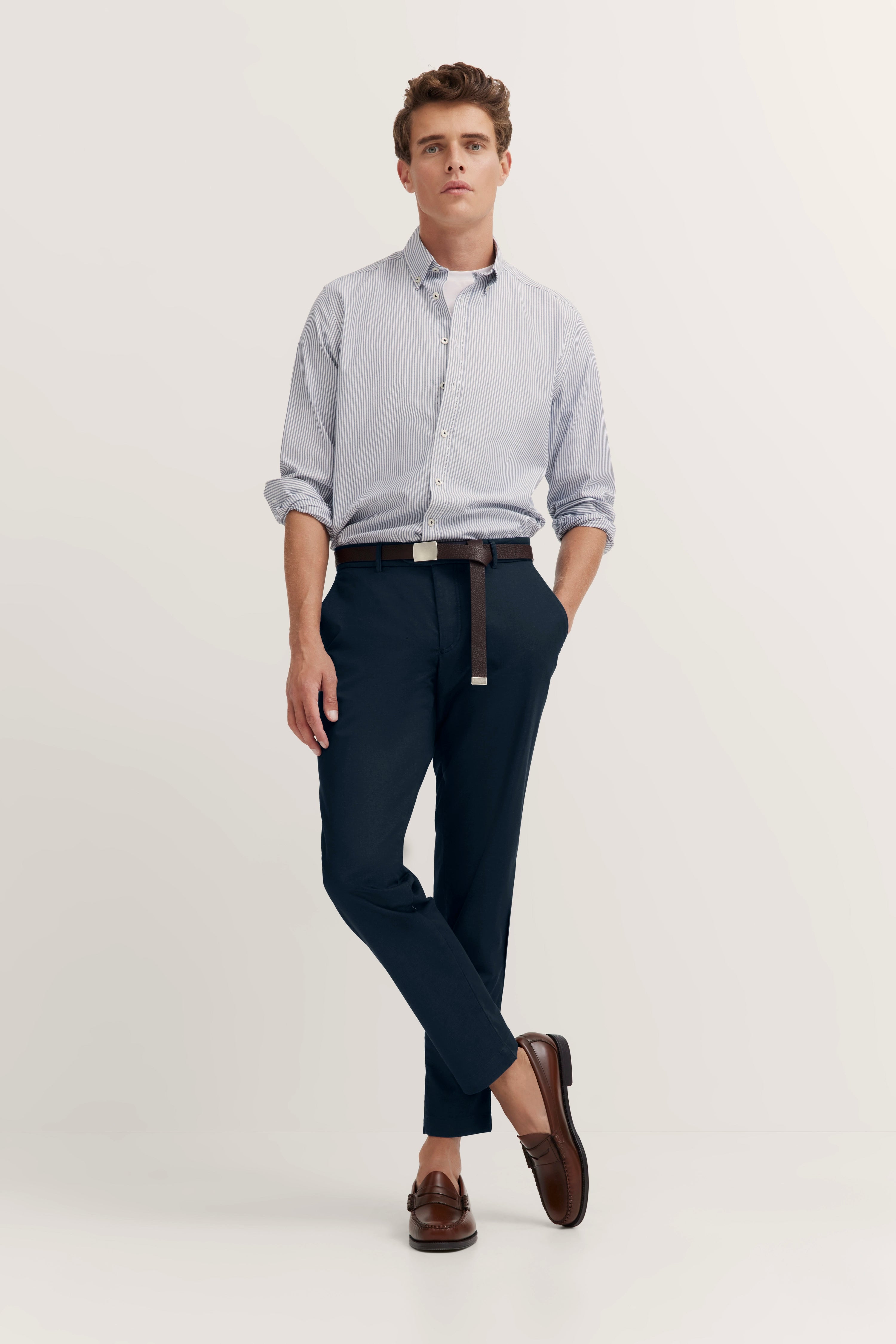 Model in smart-casual bugatti Outfit, gestreiftes Hemd, dunkelblaue Hose, braune Loafer, lässige Pose.