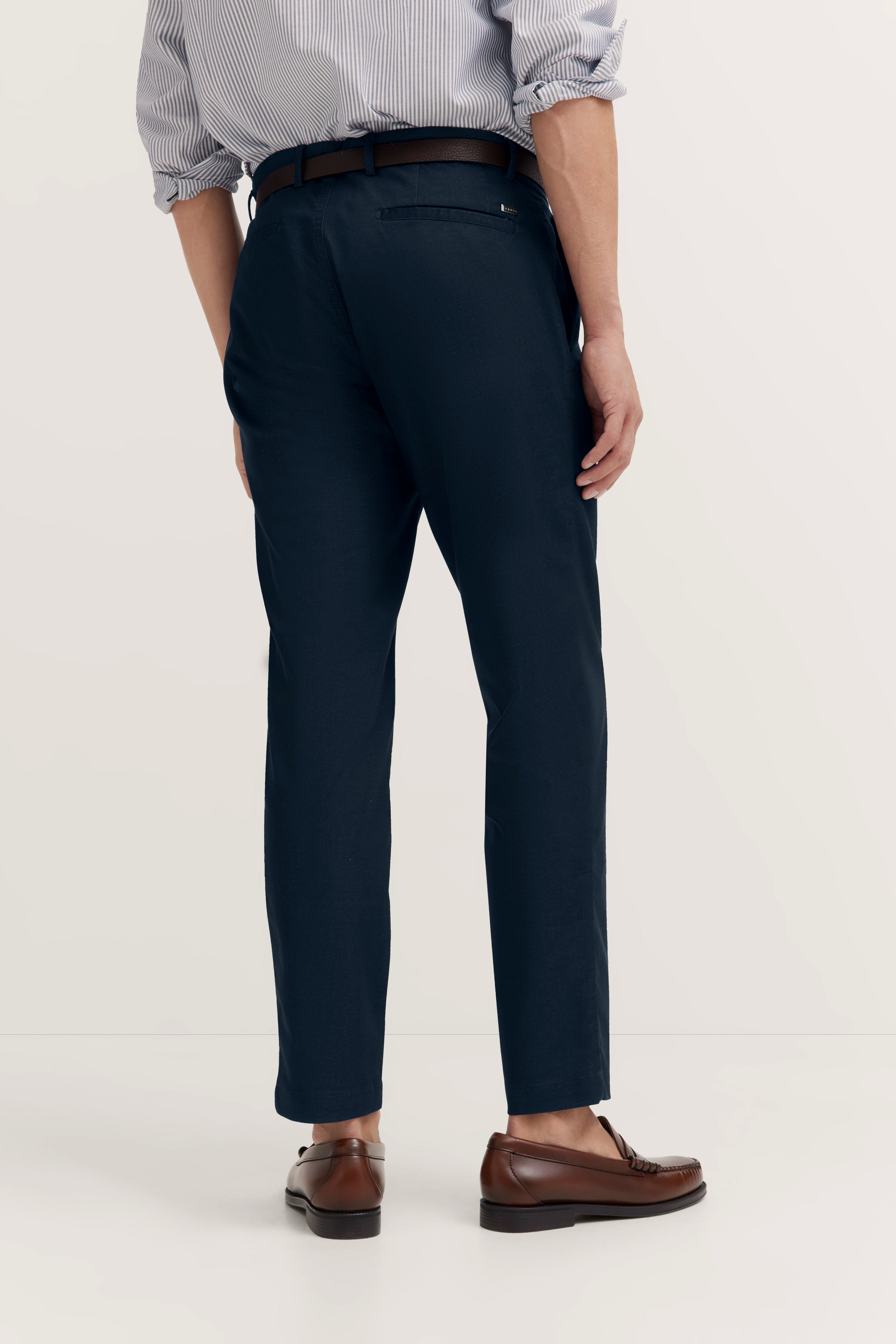 bugatti Outfit: Dunkelblaue Chinos, gestreiftes Hemd, braune Loafer. Modelbild, lässige Pose von hinten.