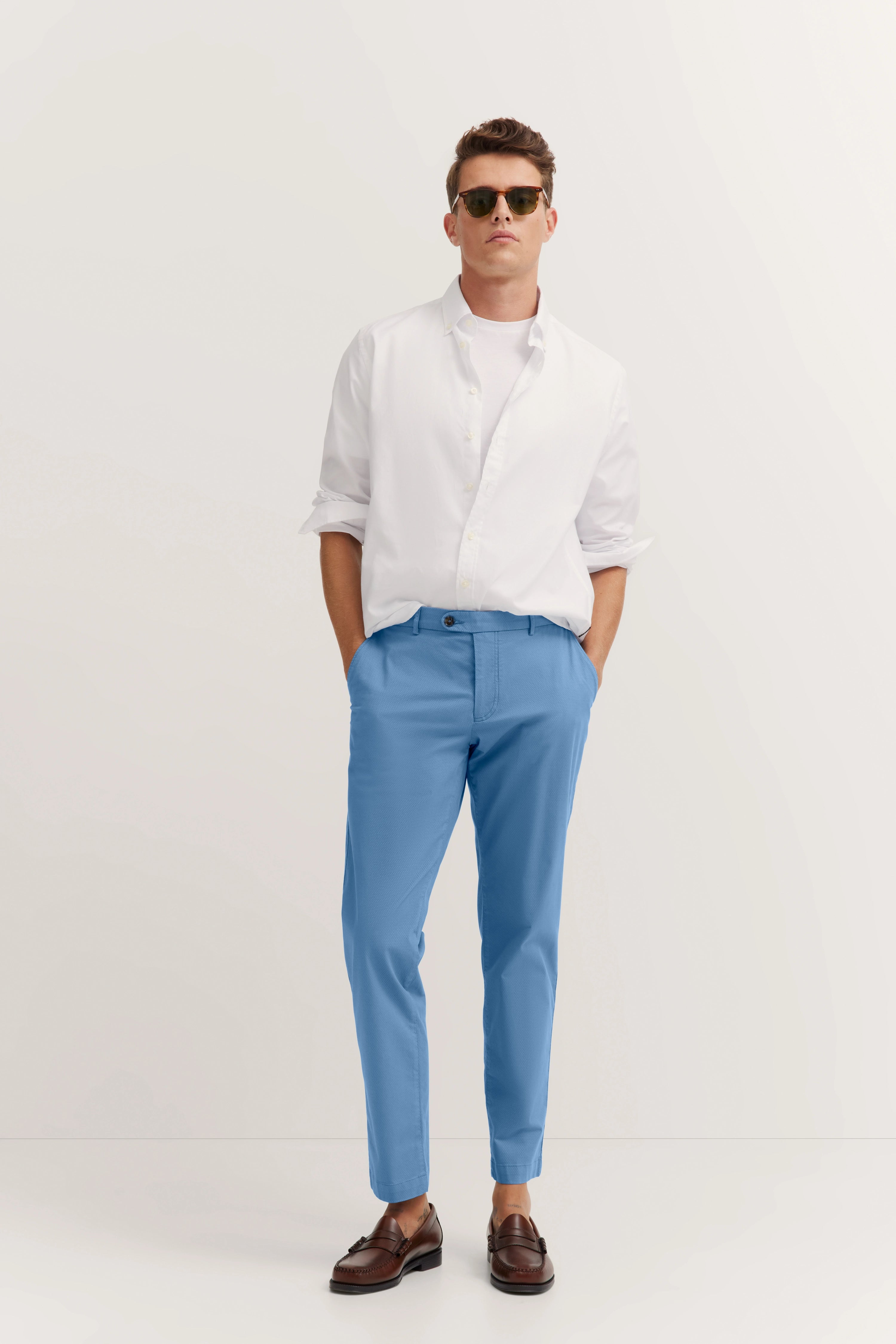 Man in lichtblauwe bugatti broek, wit overhemd, bruine schoenen