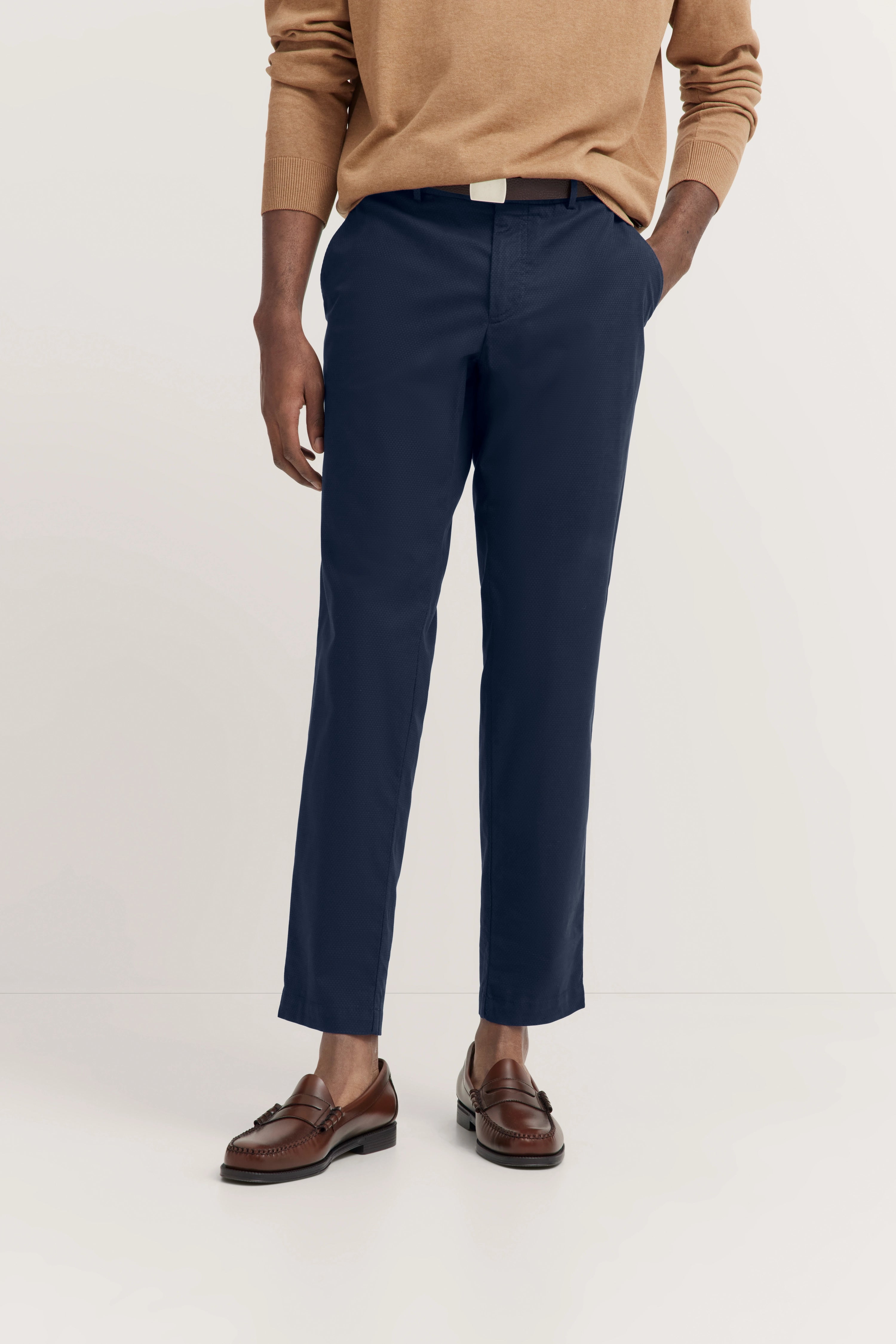 Beigefarbener Pullover, marineblaue Hose, braune Loafer. Modelbild, entspanntes Posing.