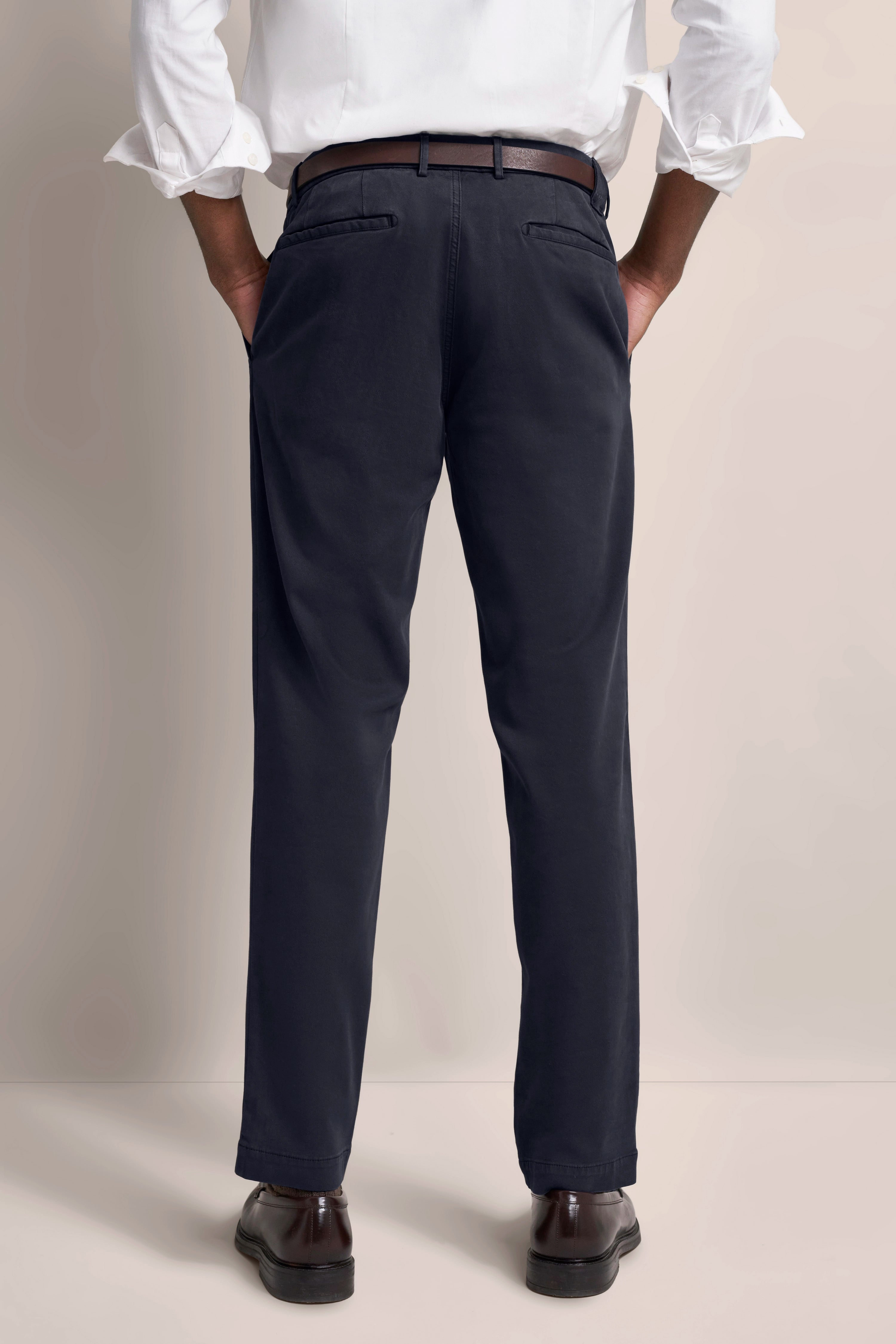 Weiße Hemd, dunkelblaue Hose, brauner Gürtel, Rückenansicht, legeres Modelbild.
