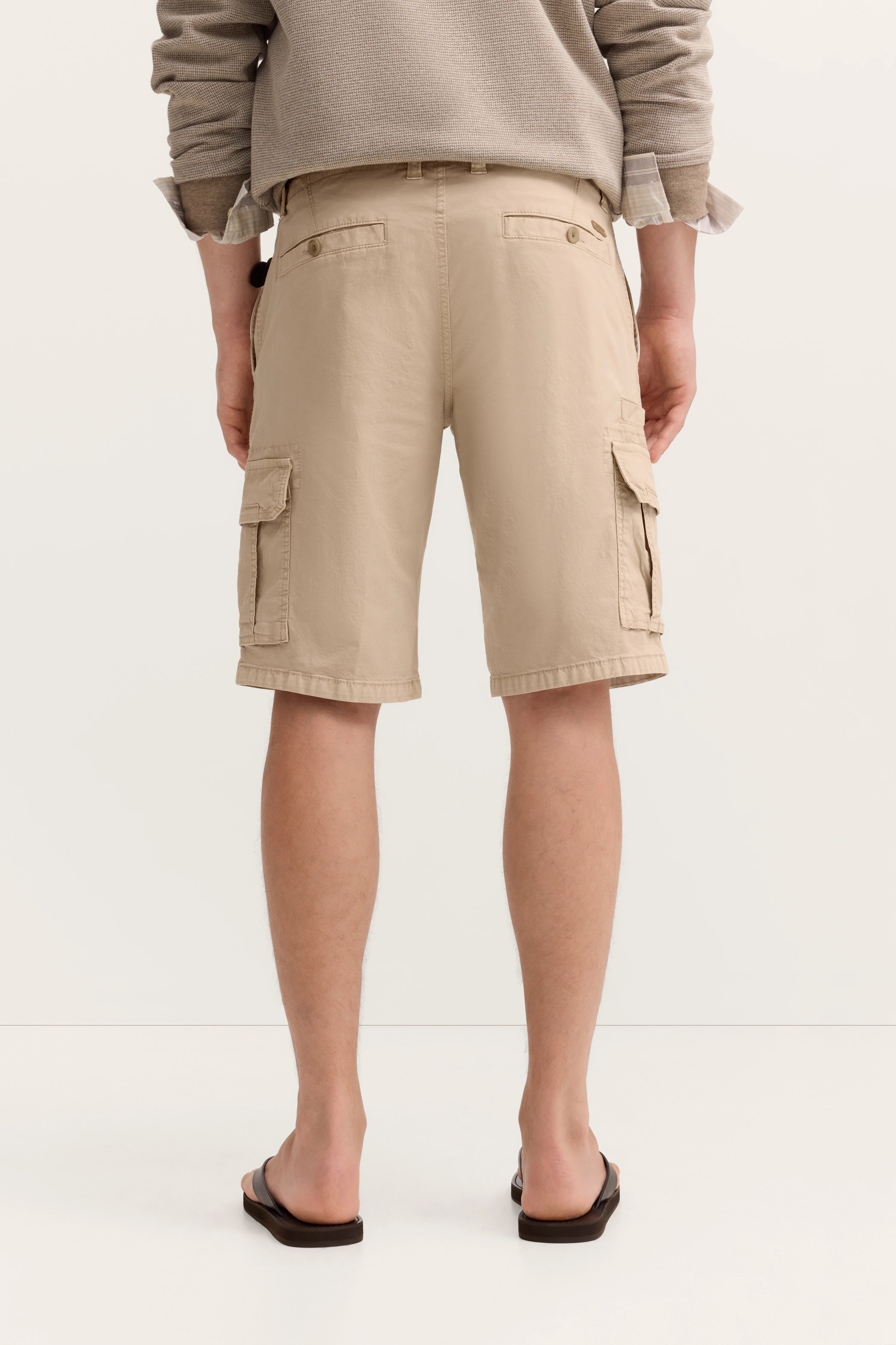 Beige Cargo-Shorts im legeren Büstenbild, kombiniert mit braunen Flip-Flops.