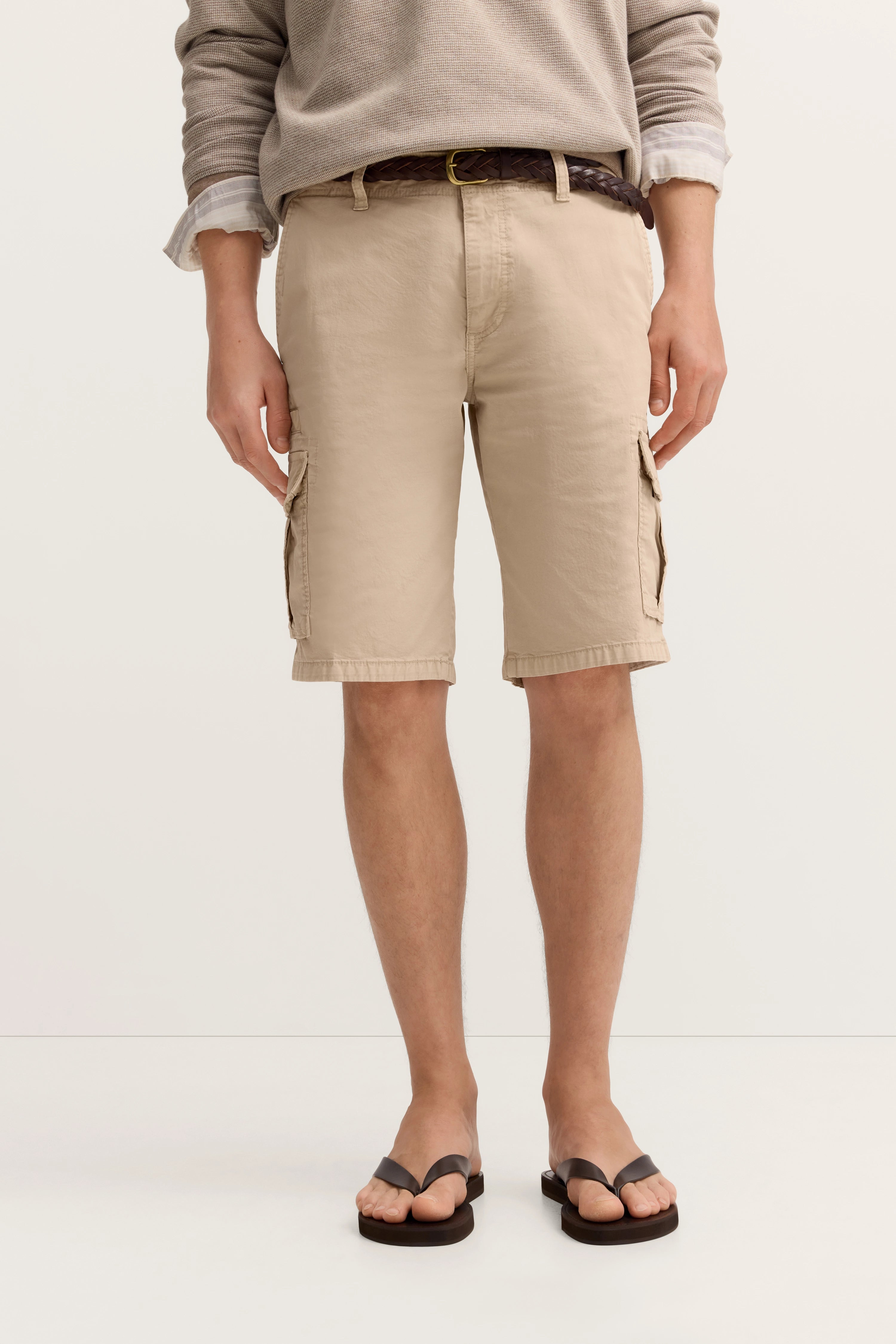 Beige Cargo-Shorts und grauer Pullover mit Flip-Flops. Legeres Modelbild, entspannte Pose.