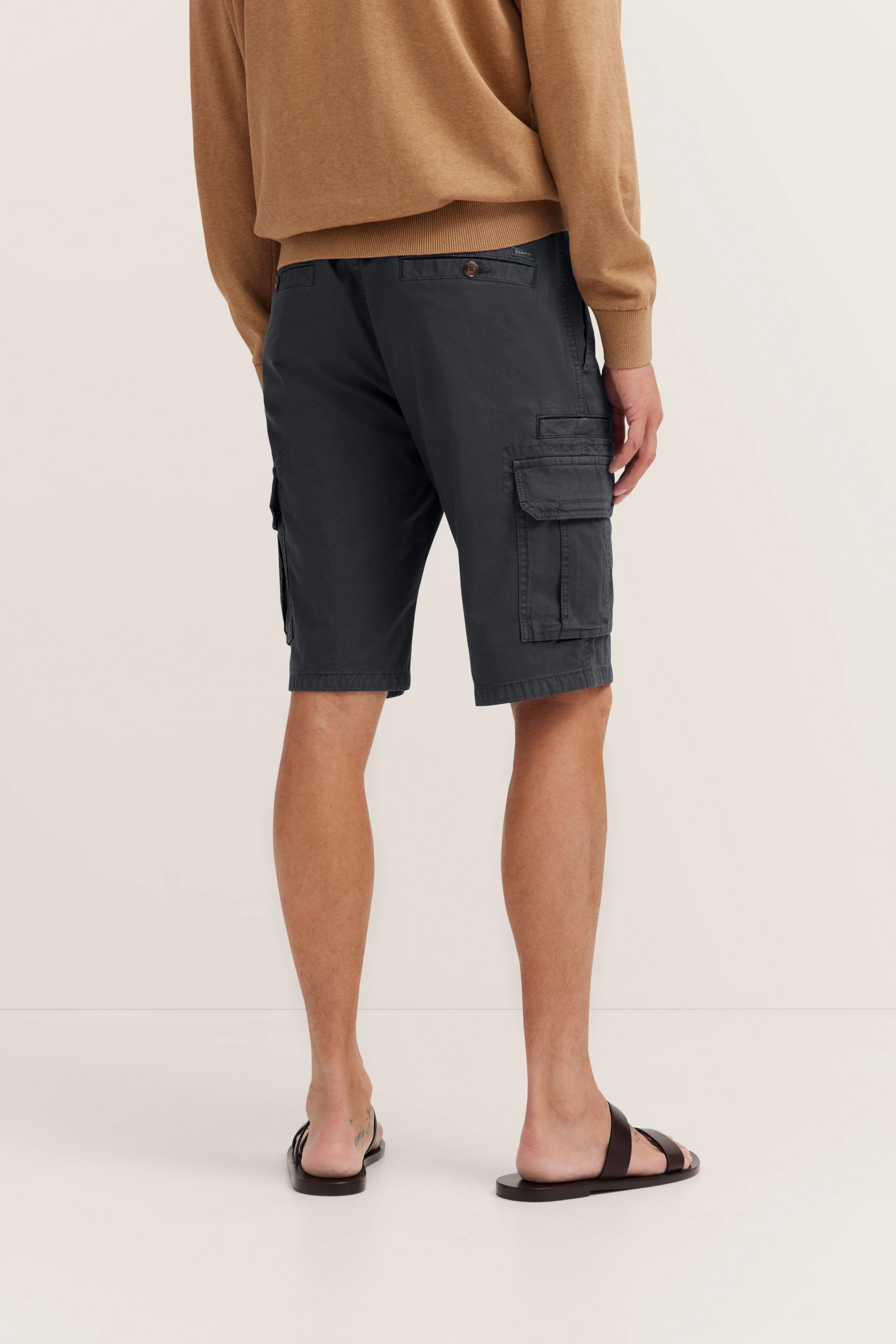 bugatti Modelbild: Beige Pullover, dunkle Cargo-Shorts, schwarze Sandalen, entspannte Rückenansicht.