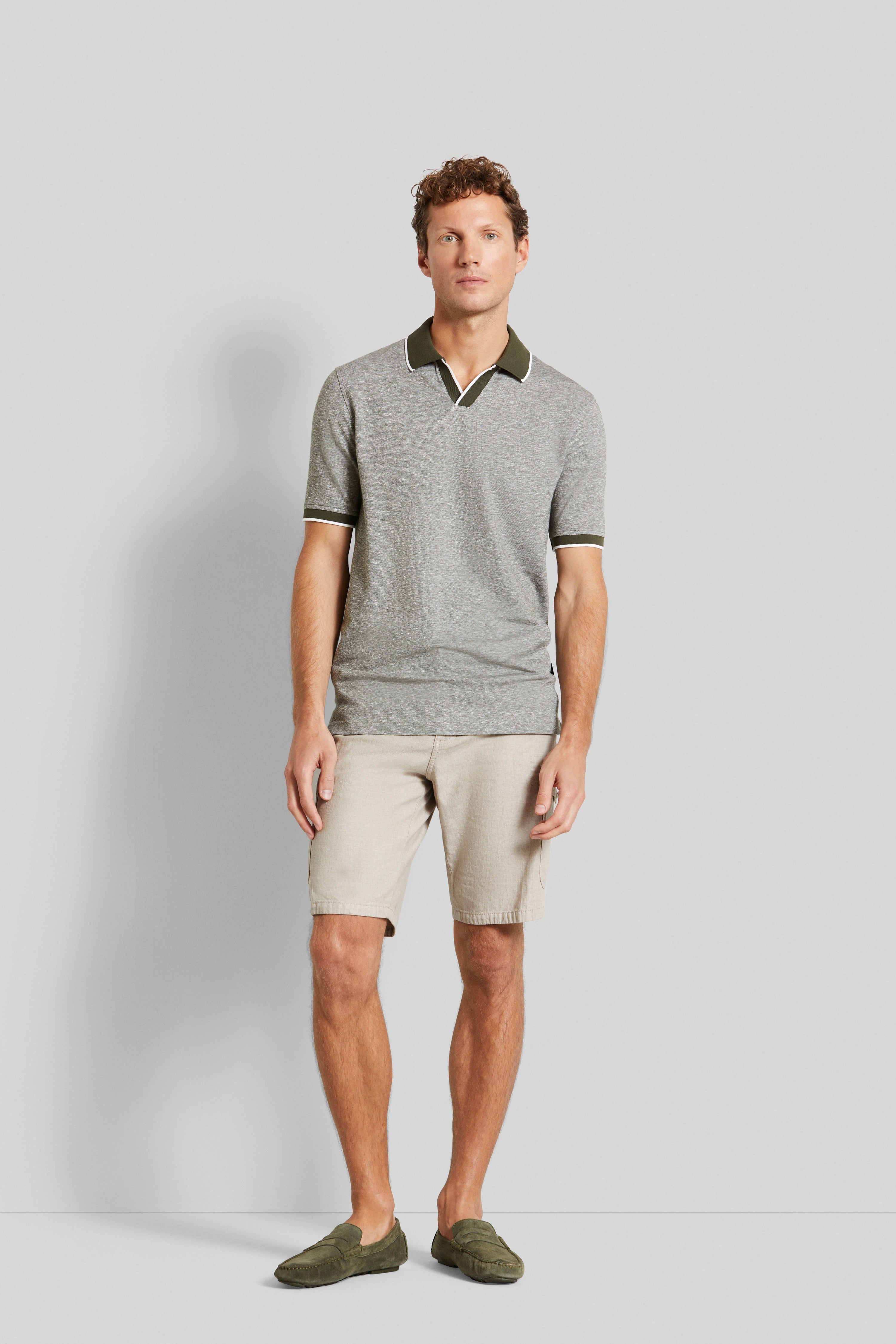 Graues Polo, beige Shorts, grüne Schuhe. Modelbild, entspanntes Posing.