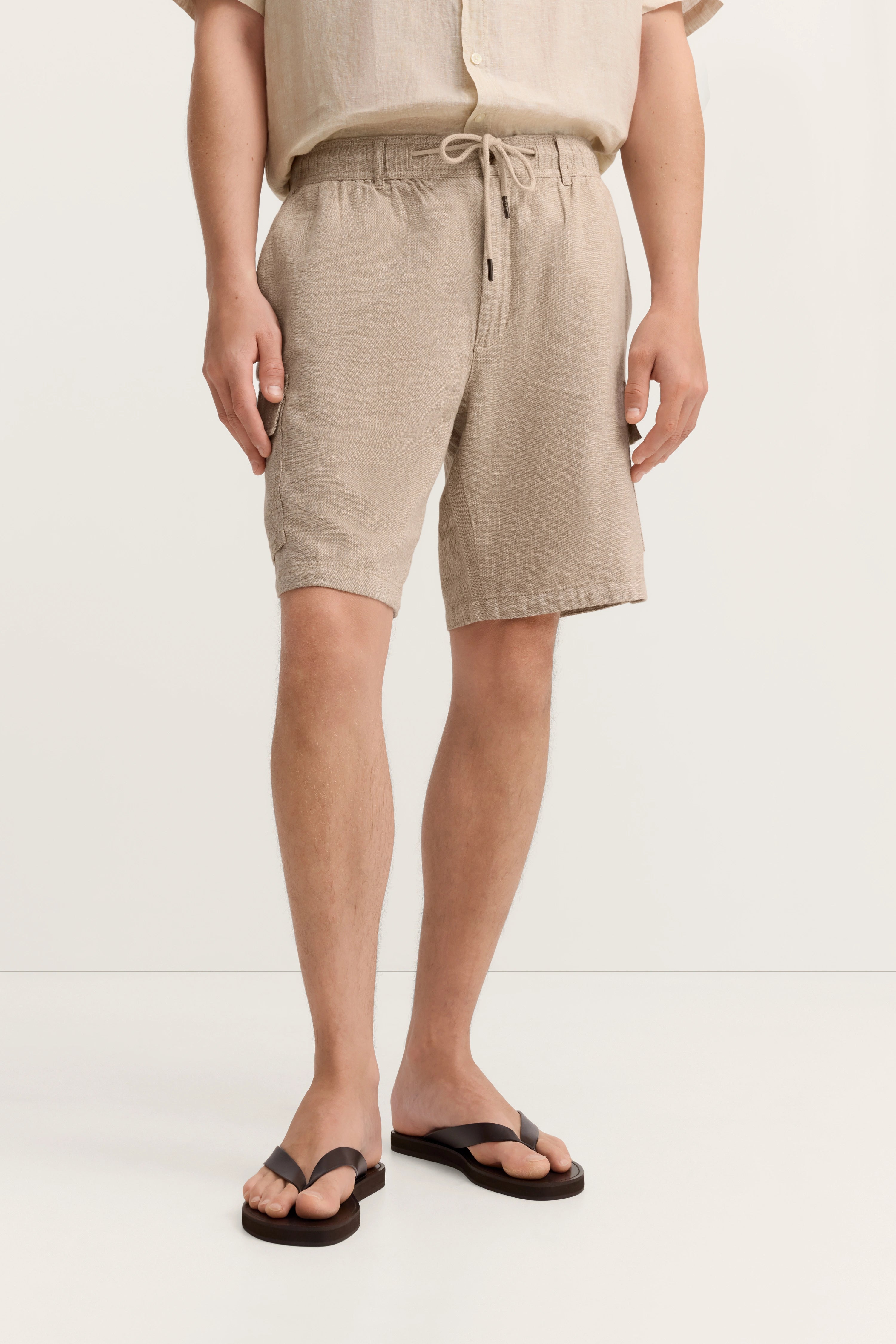 Beige Leinenhemd und Shorts, legeres Modelbild, entspanntes Posing, stilvoll mit Flip-Flops.