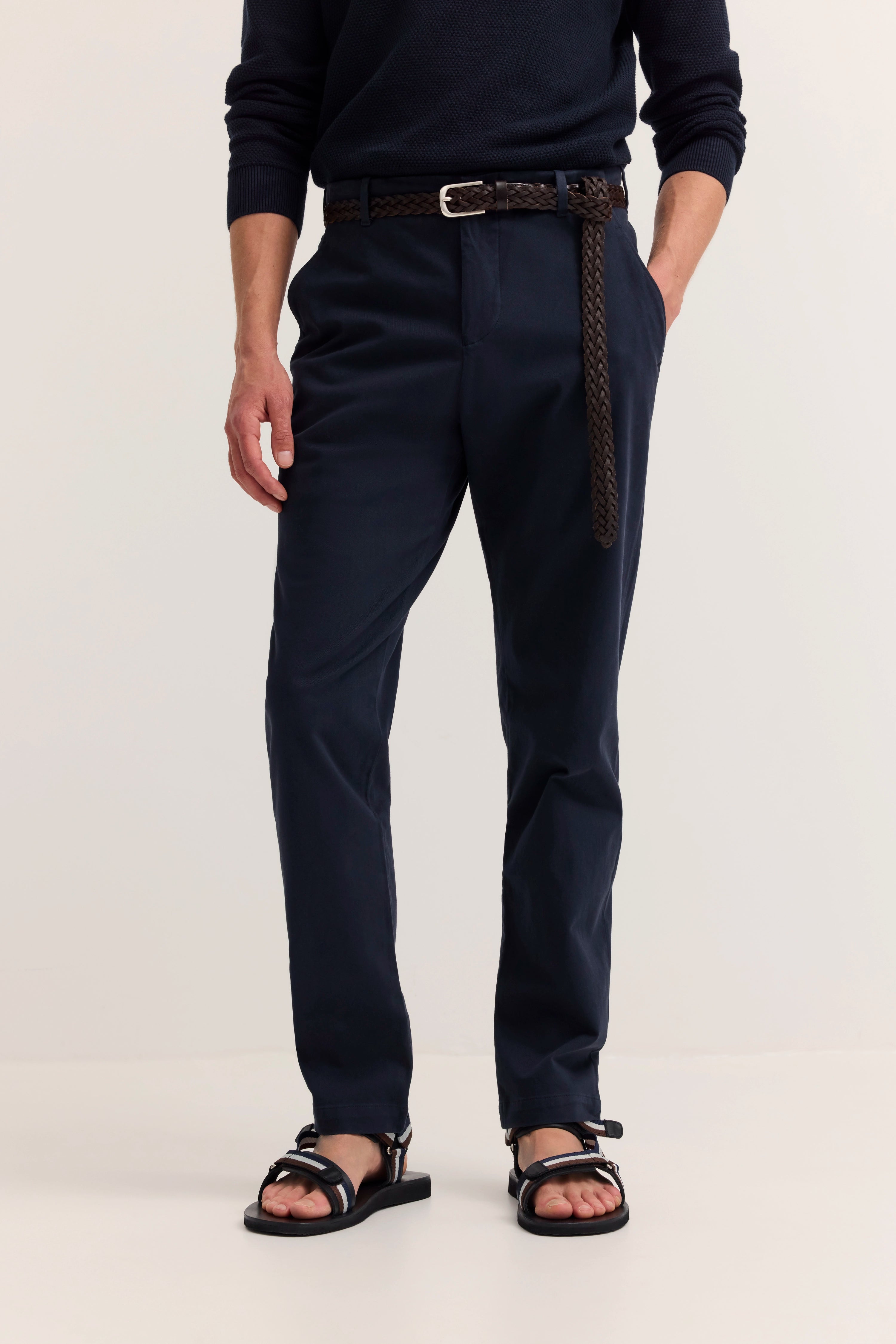 Navy Chinos mit Flechtgürtel und Sandalen, legeres Modelbild, entspannte Pose.