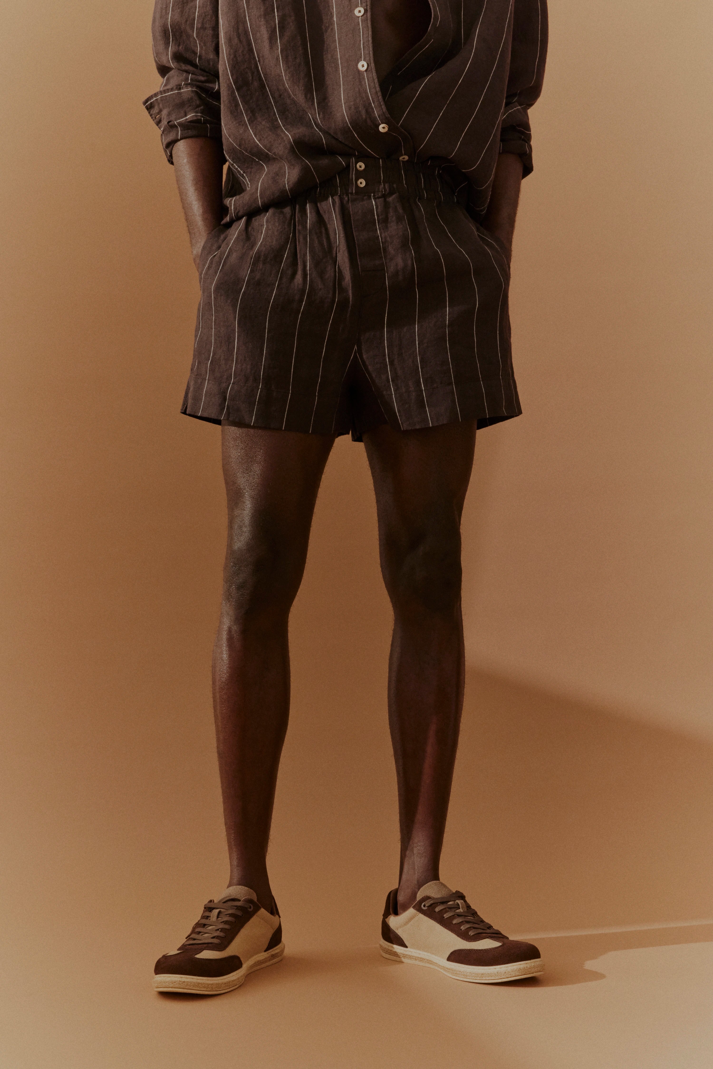 Braunes Nadelstreifen-Shorts-Outfit, legeres Modelbild, Hände in Taschen, Freizeitlook.
