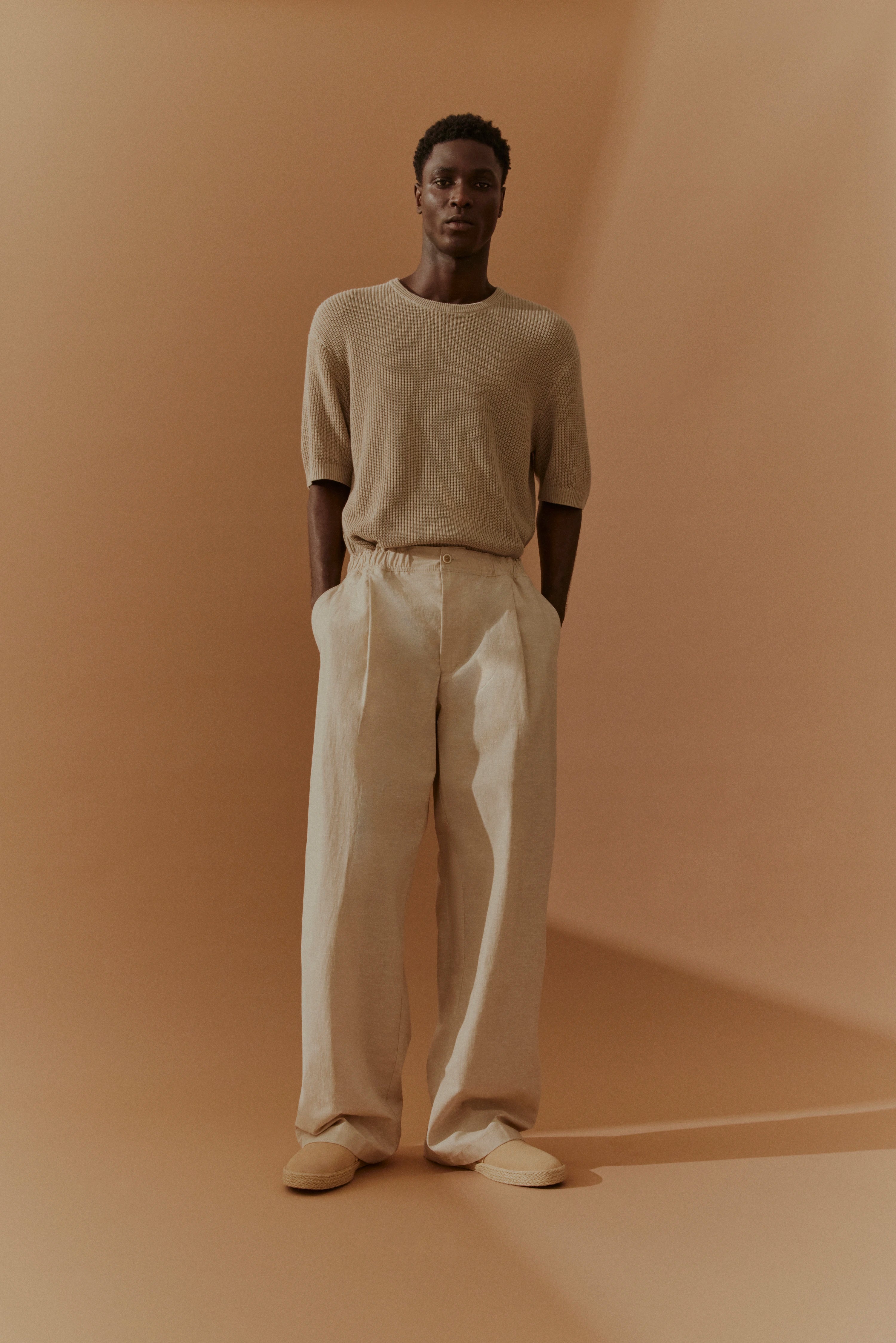 Model in beige bugatti Outfit, T-Shirt und weite Hose, legeres Posing.