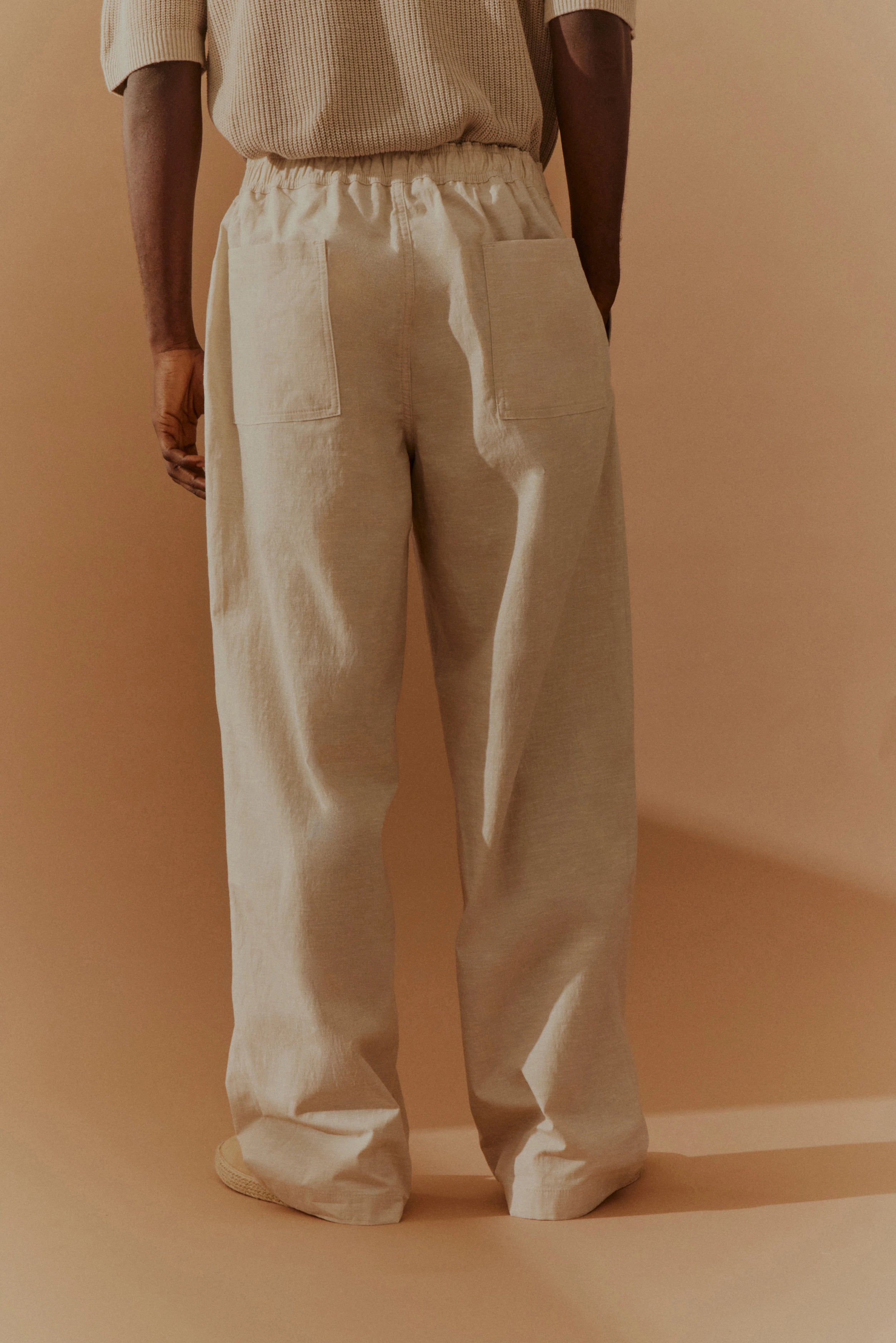 Beiges Outfit mit lockerem Pullover und weiten Hosen, Modelbild von hinten, entspannte Pose.