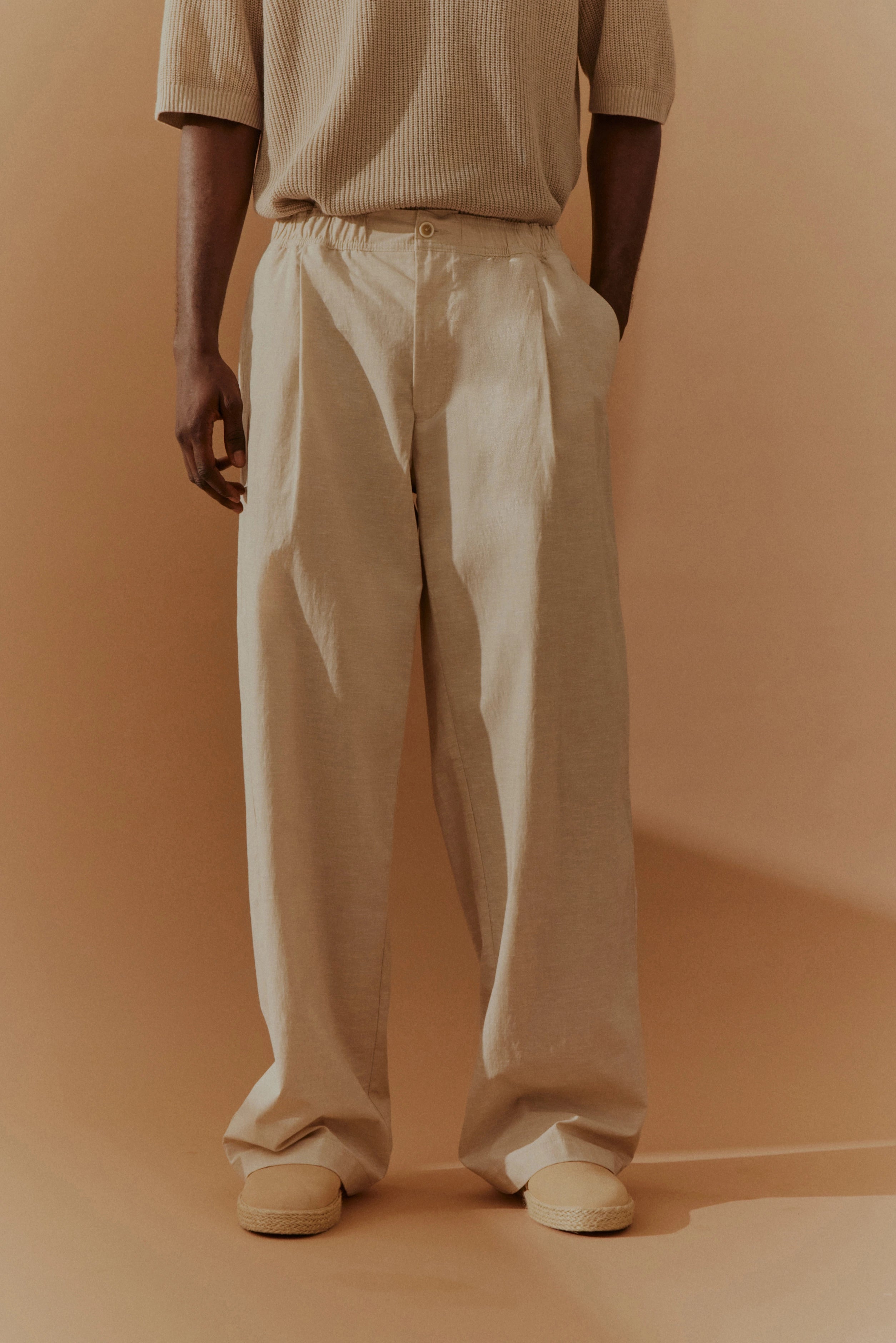 Beiger Pullover und weite Hose, Model steht leger, beige Hintergrund, bugatti Stil.