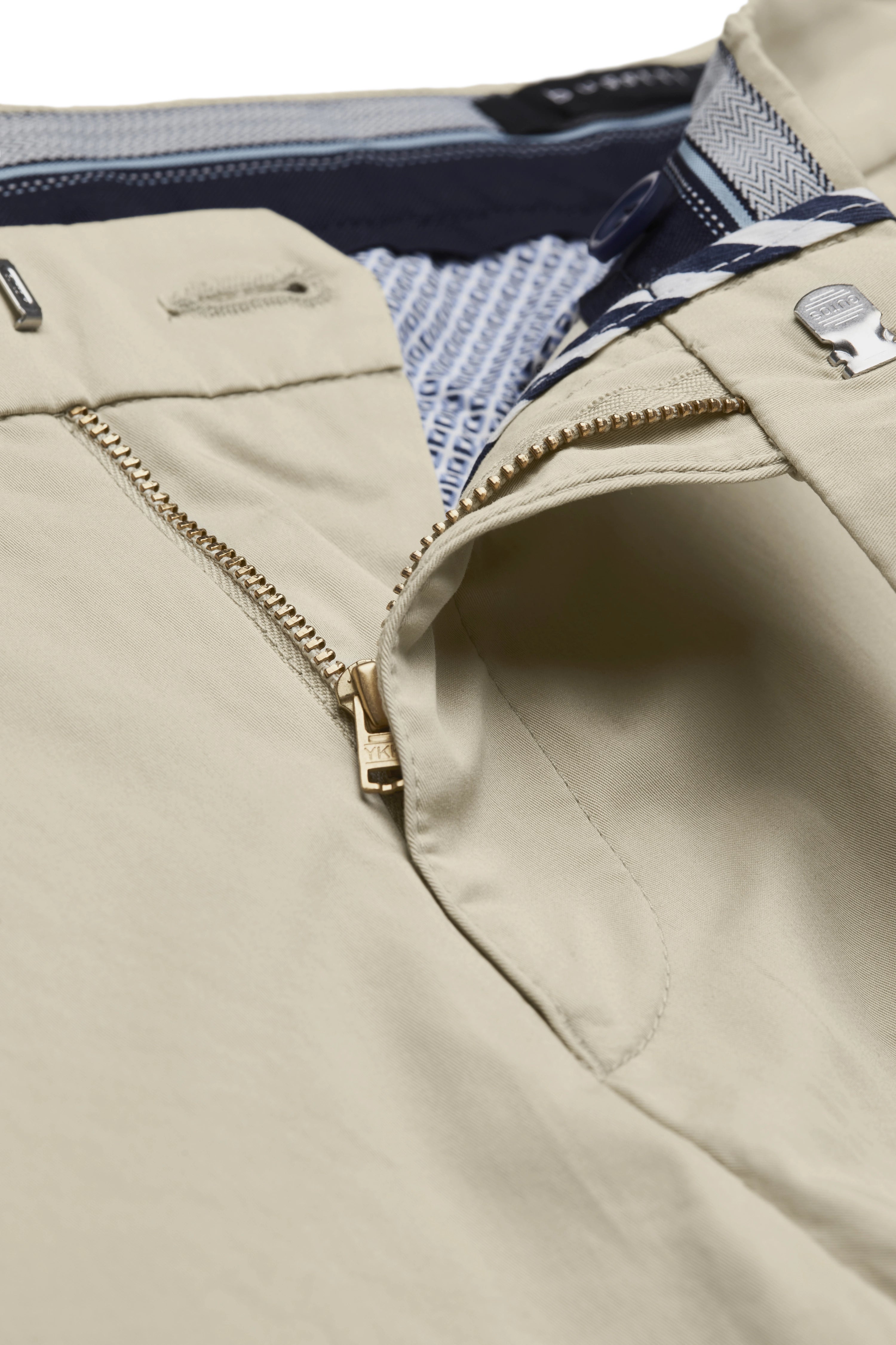 Beige bugatti broek close-up met goudkleurige rits en gevoerd patroon aan de binnenkant.