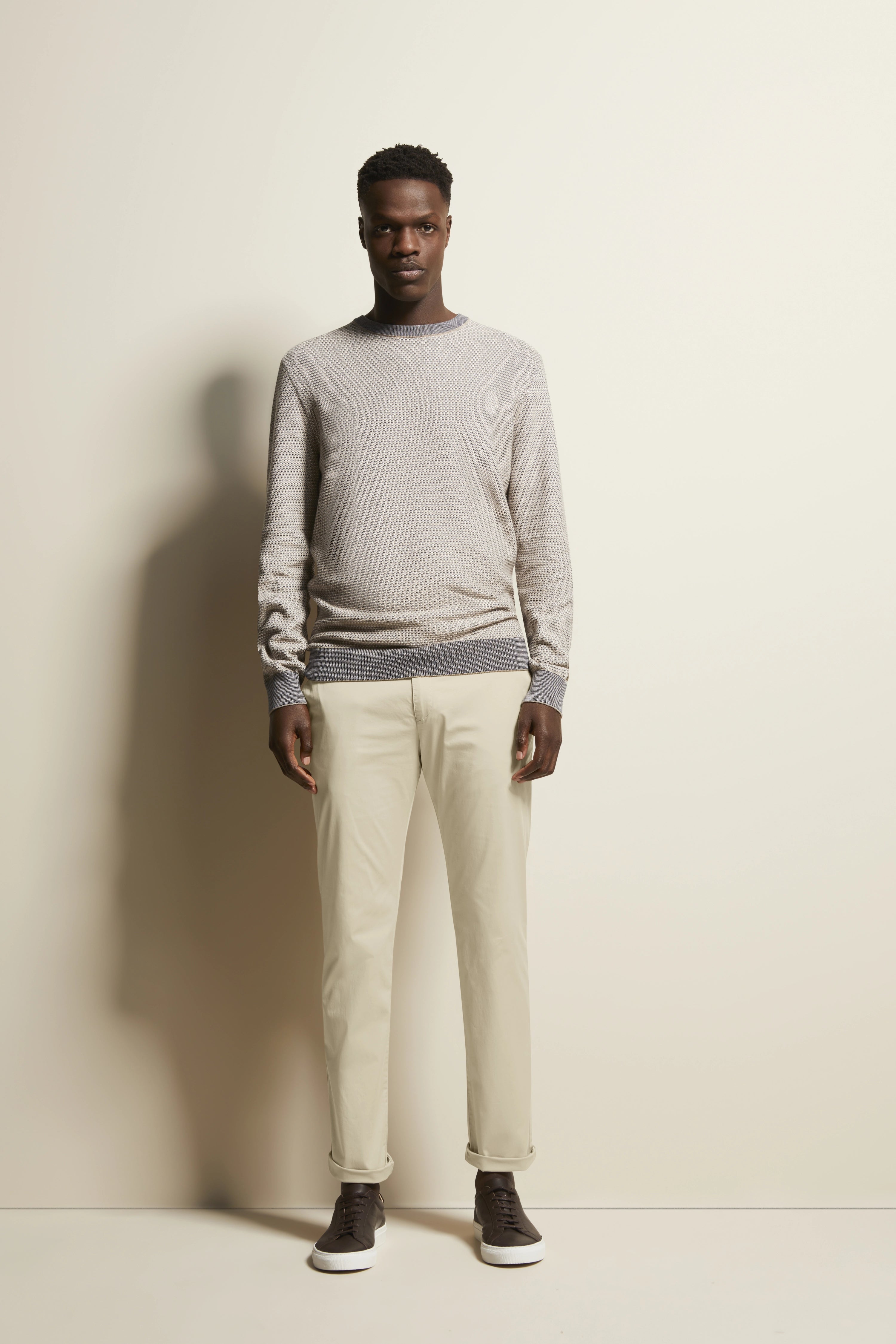 Model in beige bugatti trui en chino, casual staand, bruine sneakers.