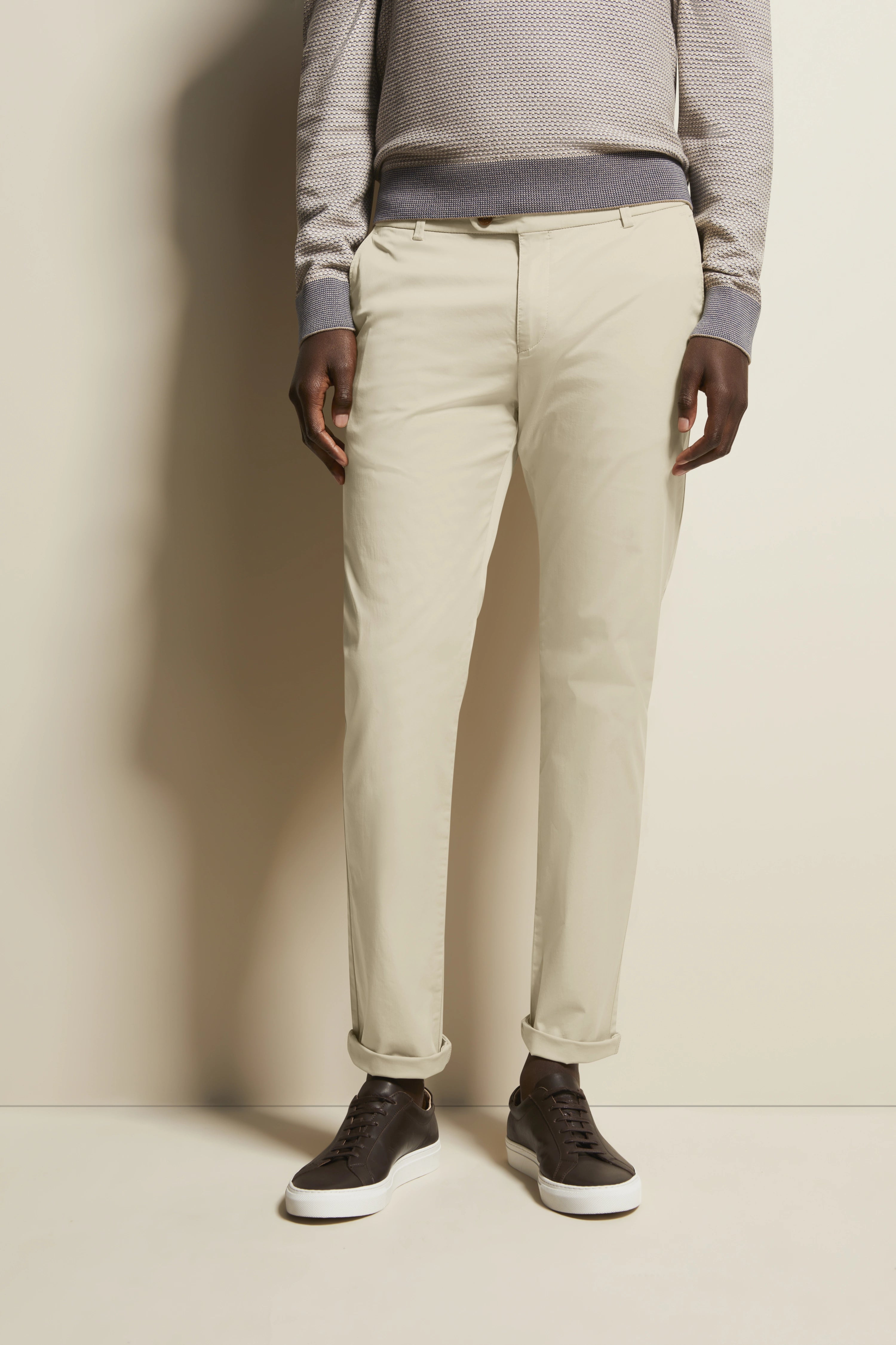 Beige chino met grijze trui, bruine sneakers. Model in ontspannen houding. bugatti stijl.