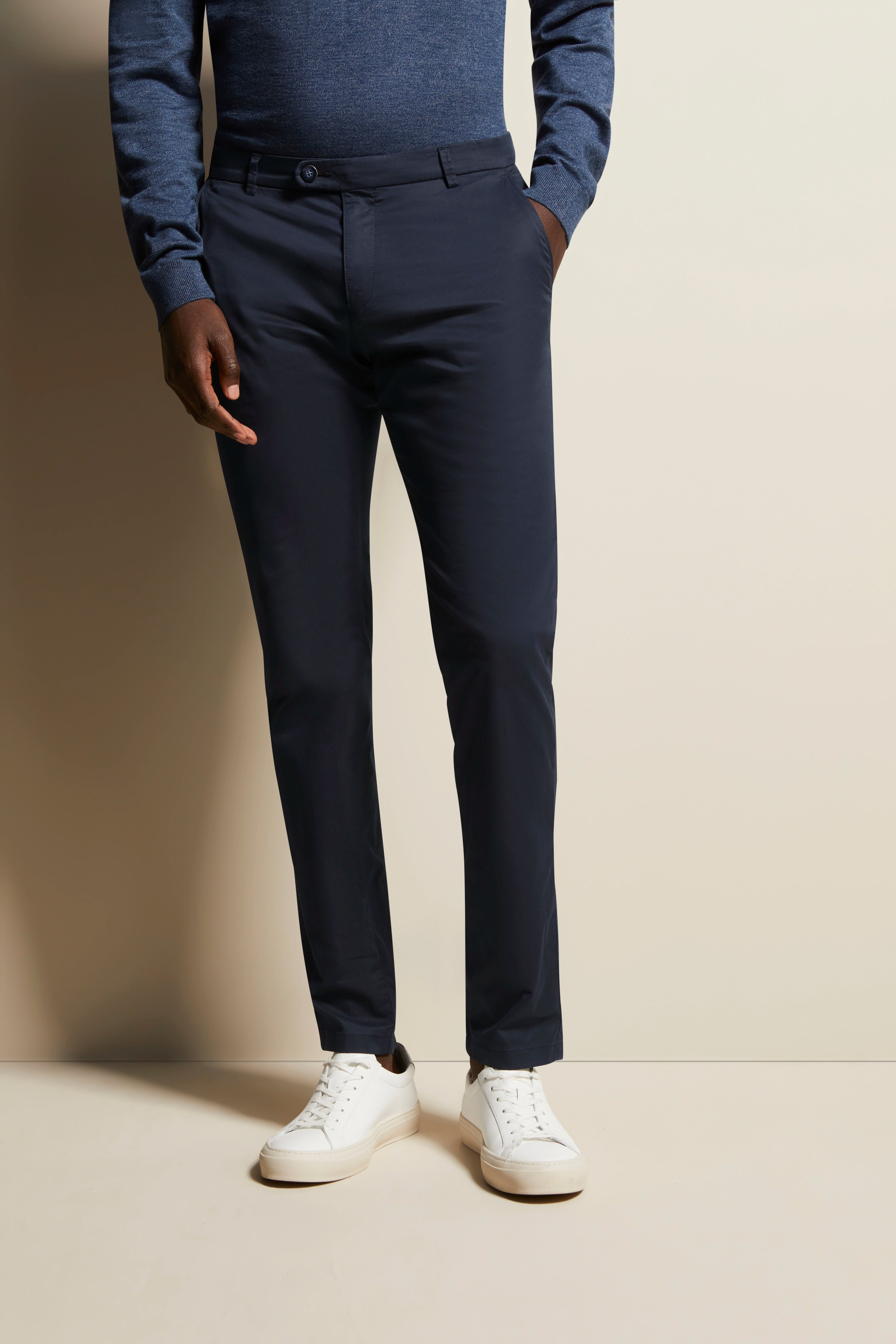 Navy chino en blauwe trui, casual modelbeeld, staande pose, witte sneakers.