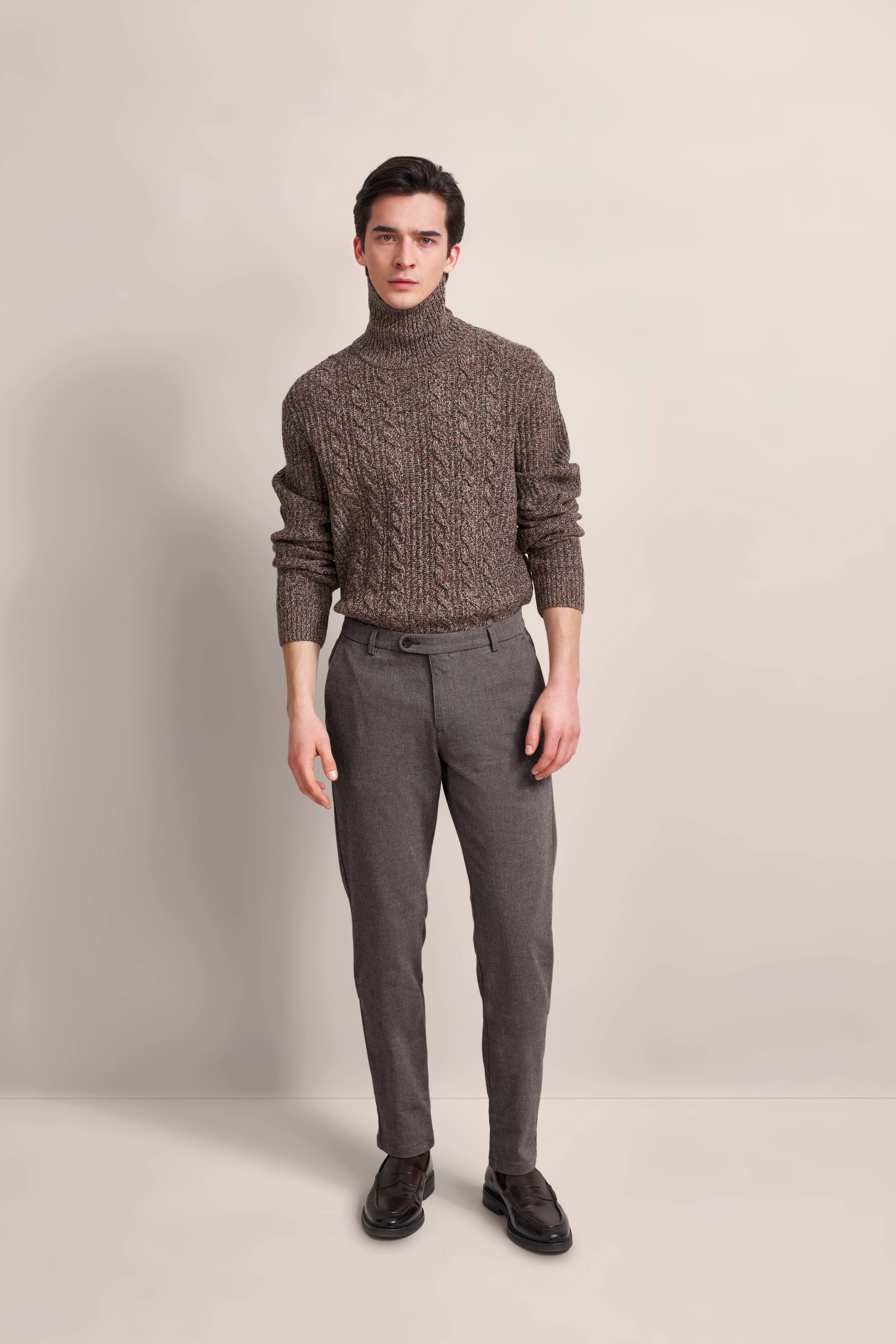 Model trägt braunen Rollkragenpullover und graue Hose von bugatti, lässige Pose.