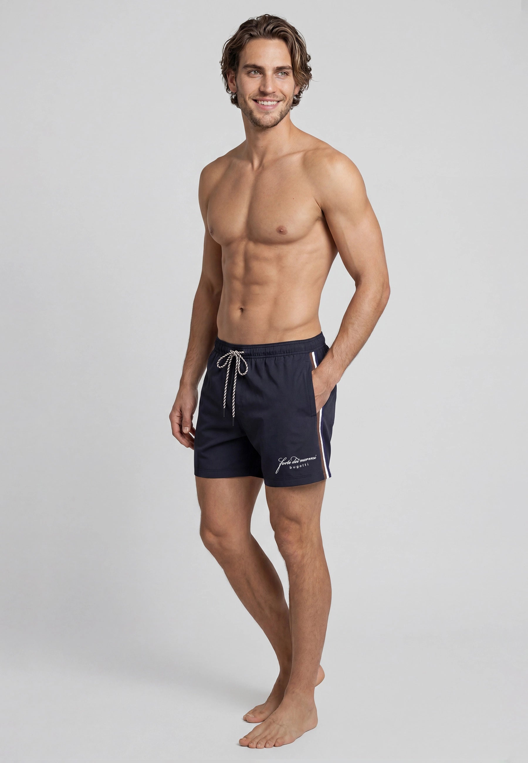 Model in dunkelblauer bugatti-Badeshorts, lässige Pose, entspannter Ausdruck.