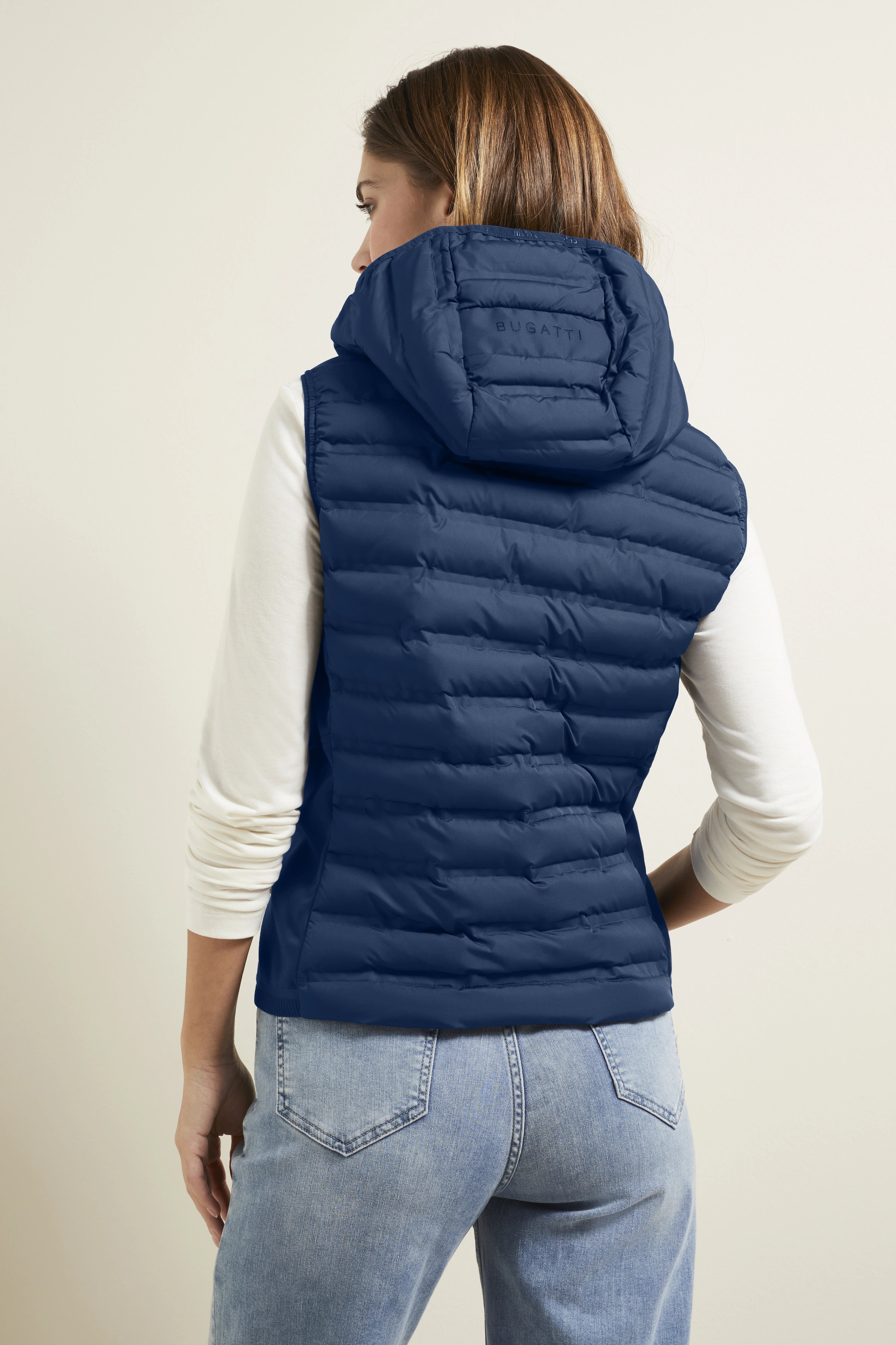 Vrouw in blauwe bugatti gewatteerde bodywarmer en jeans, rugaanzicht, casual modelbeeld.