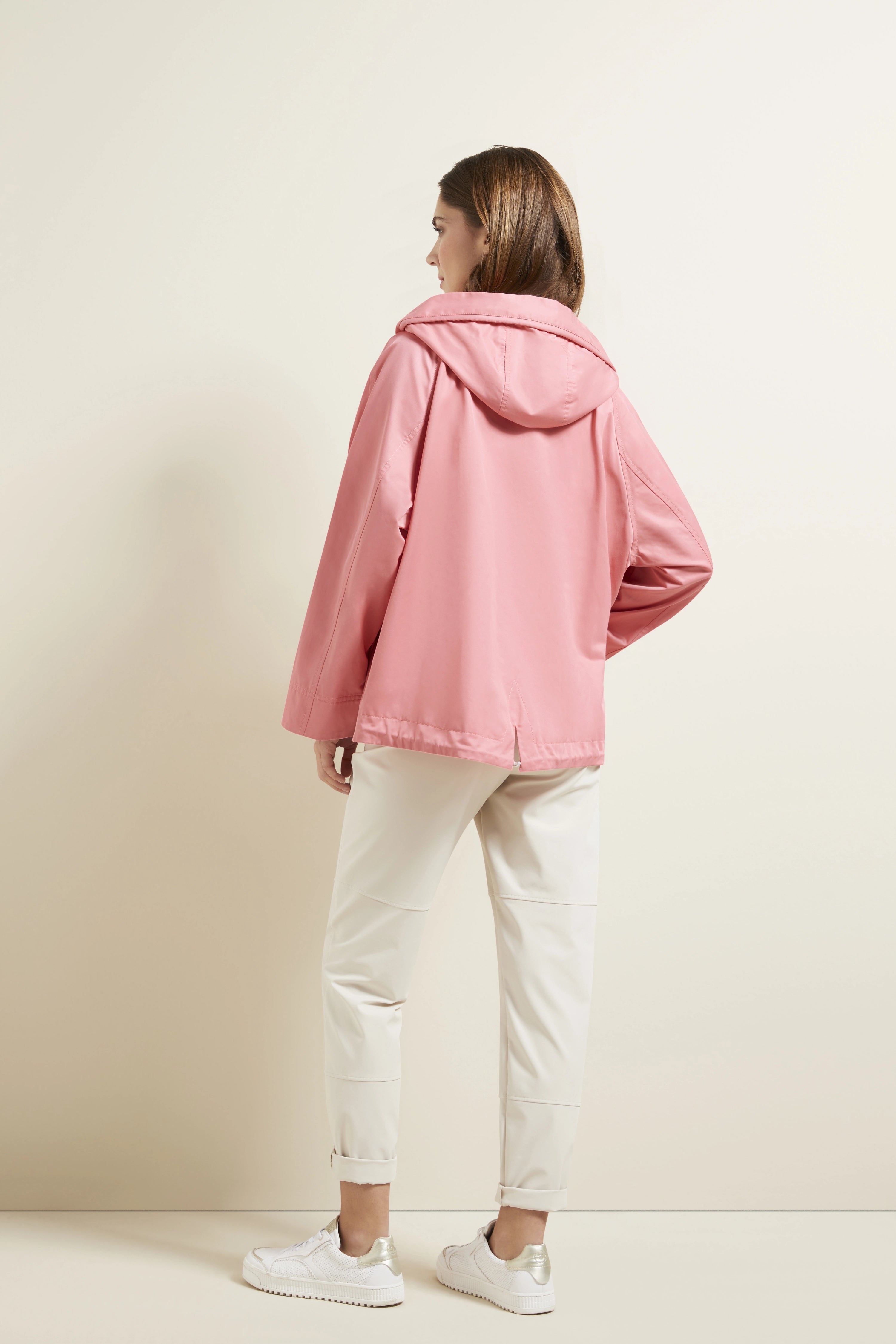 Model in rosa bugatti-Jacke, weiße Hose und Sneaker. Rückenansicht, entspanntes Posing.