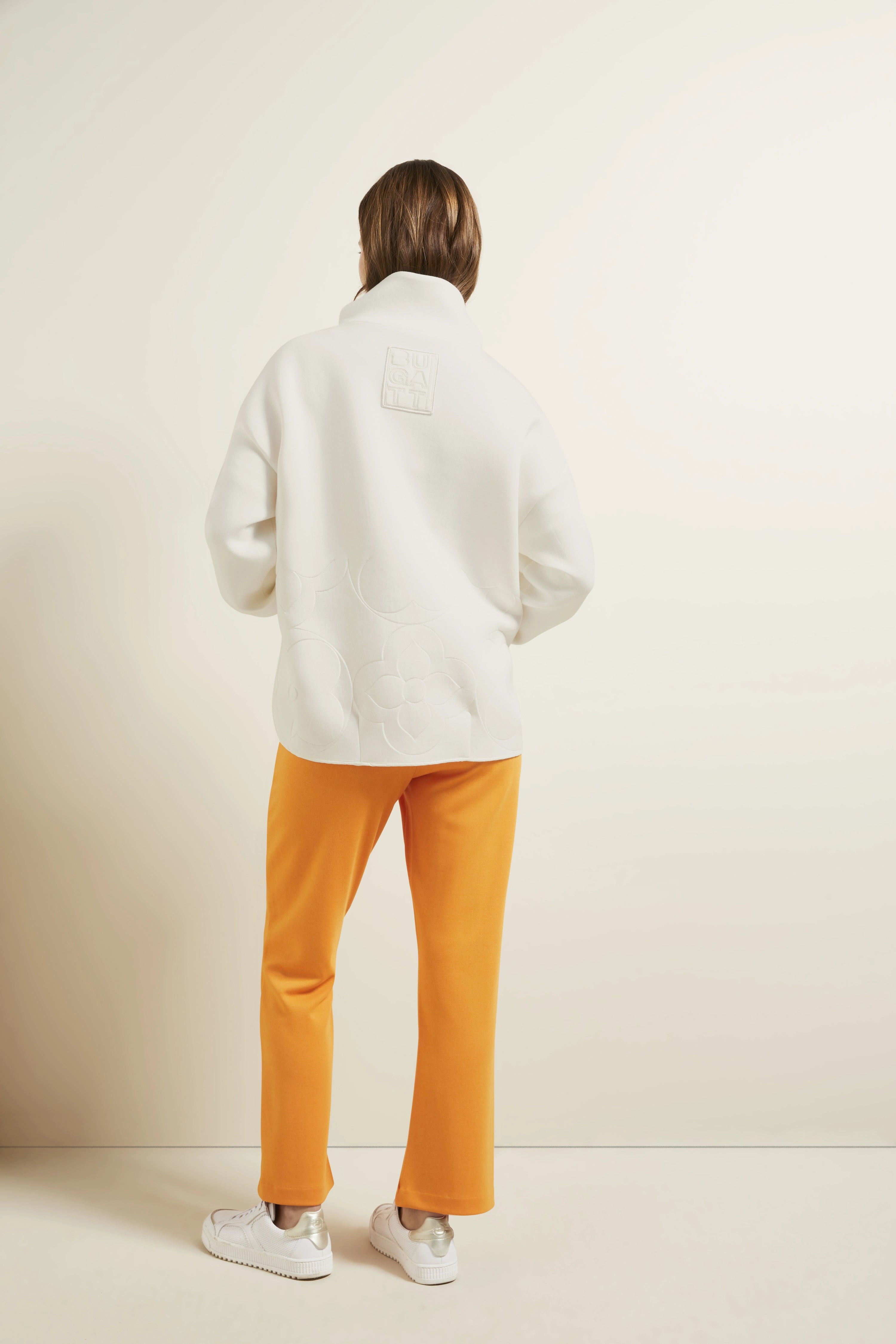 Modelbild: Weißer Pullover, gelbe Hose, weiße Sneaker. Rückansicht, entspanntes Posing.