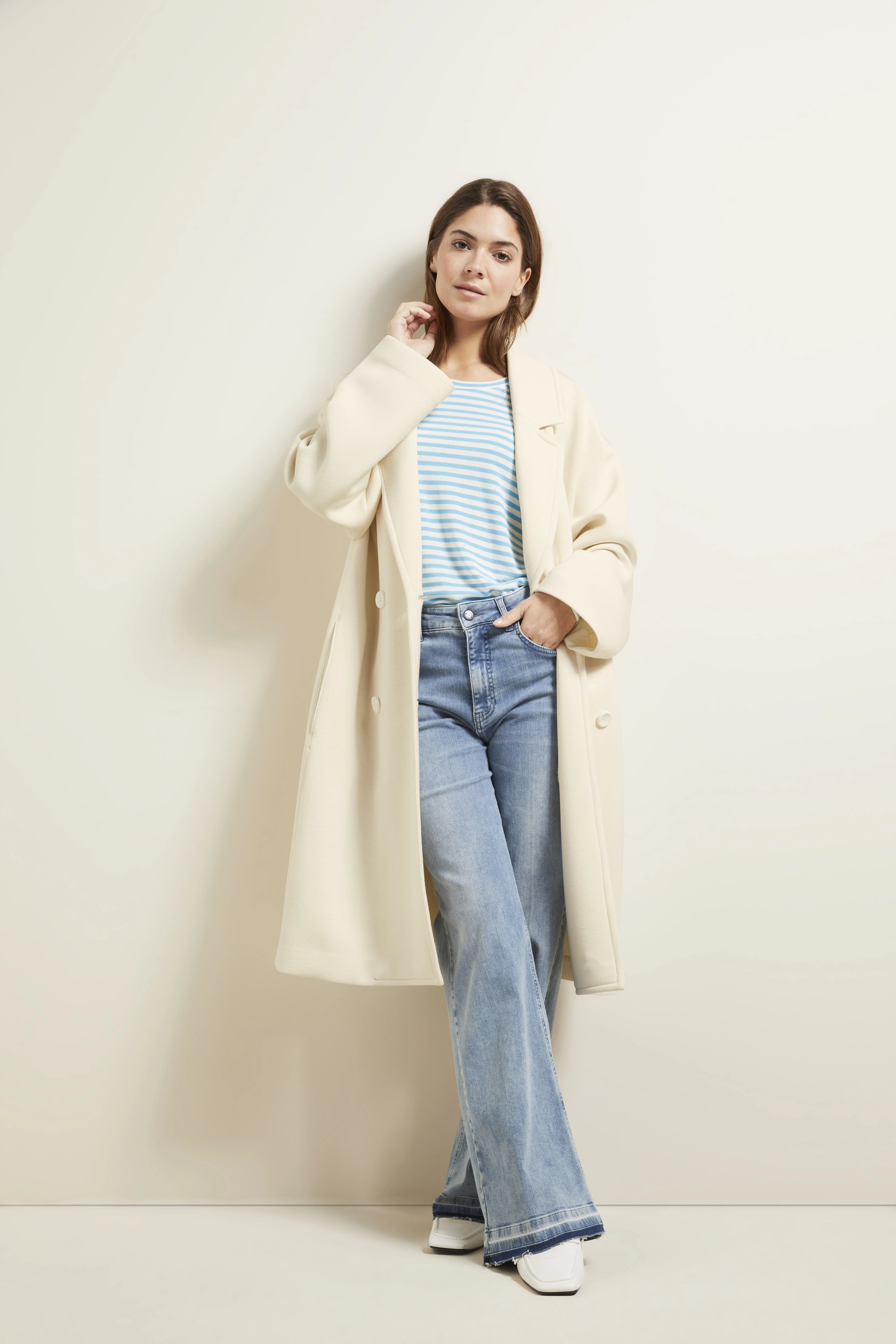 Model in cremefarbenem Mantel, blau-weiß gestreiftem Shirt, Jeans
