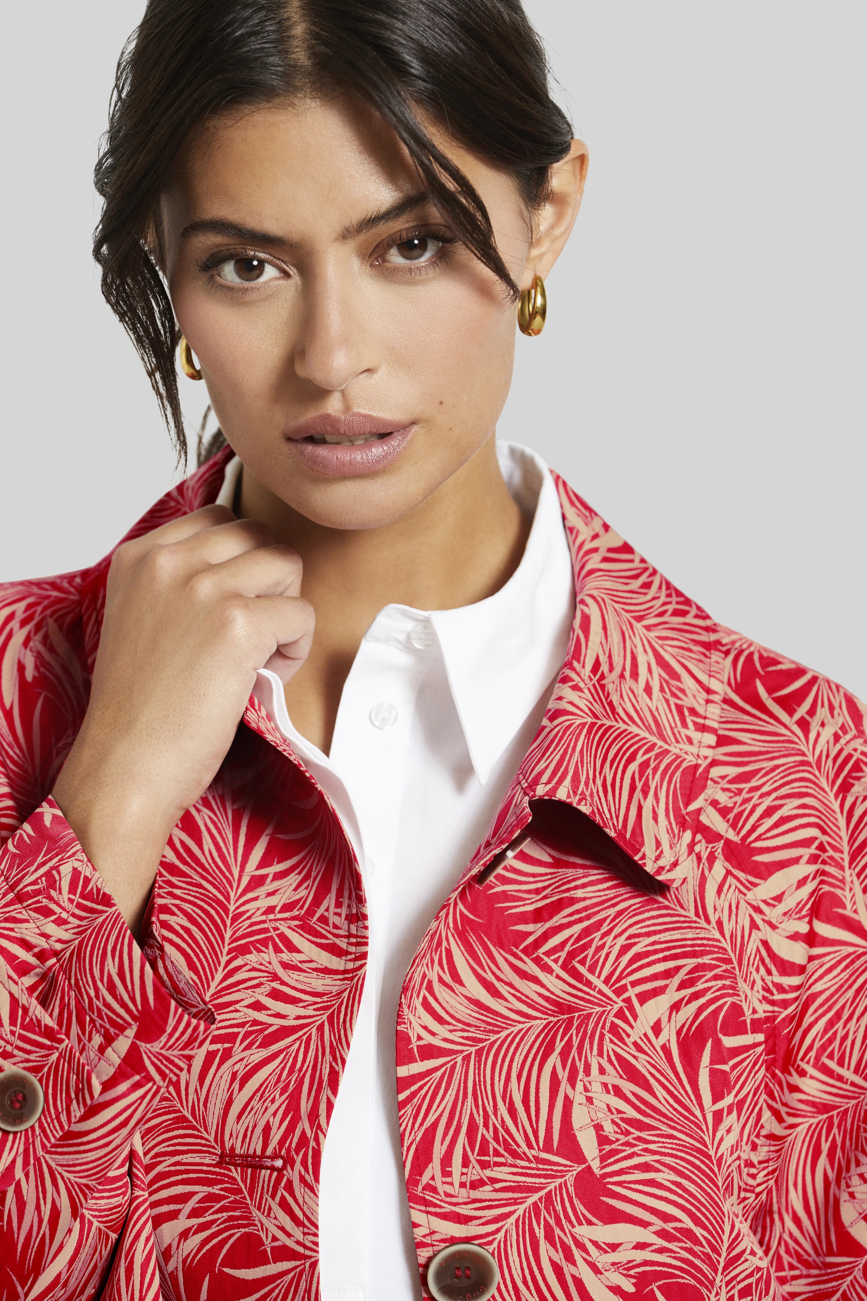 Modelbild mit rotem bugatti-Jacke mit Blattmuster, weißem Hemd, goldenen Ohrringen, elegantes Posing.