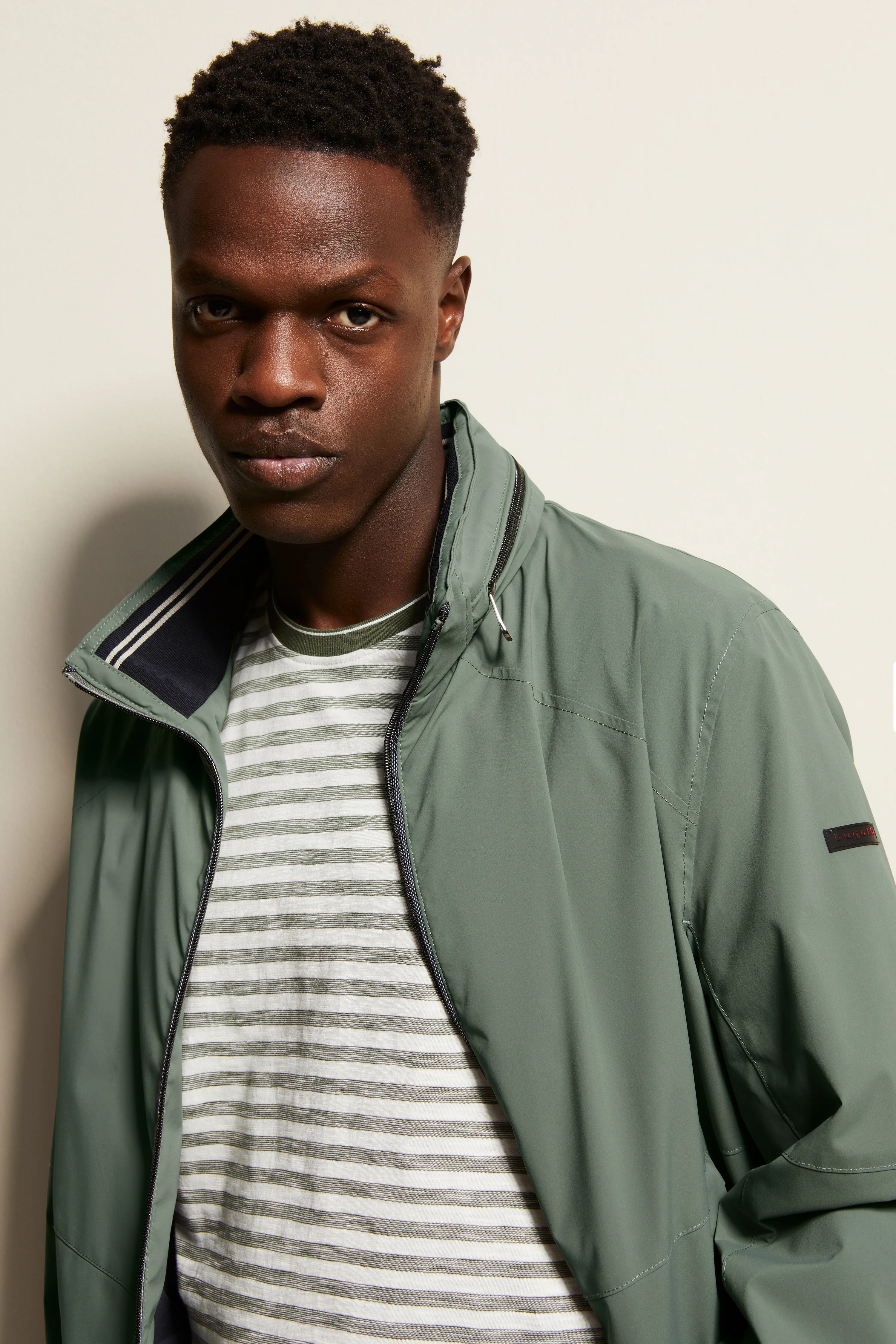 Grünes bugatti Jacket mit gestreiftem Shirt, legeres Modelbild, entspannter Gesichtsausdruck.