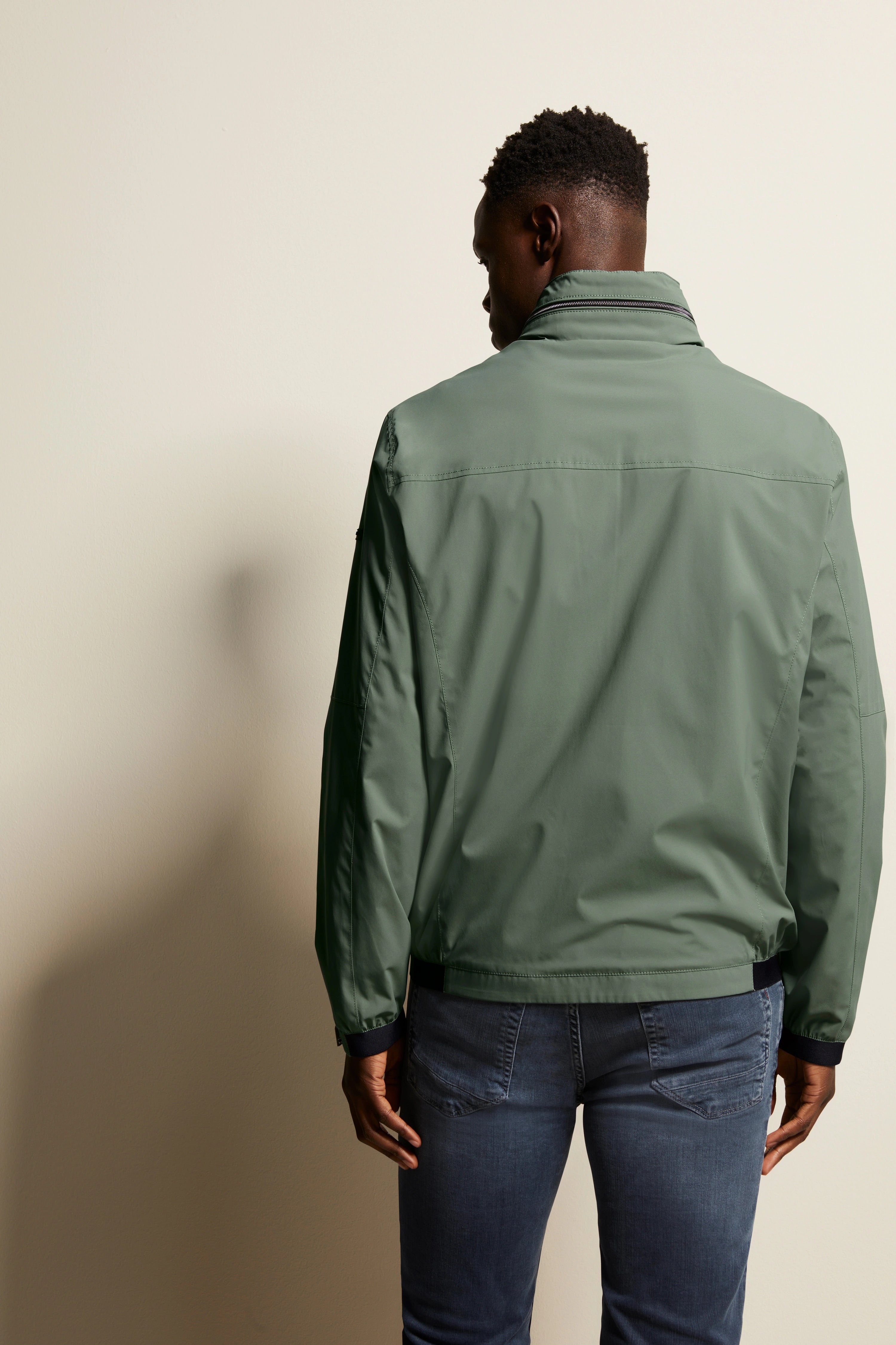 Grüne bugatti Jacke, legeres Modelbild von hinten, mit blauen Jeans.