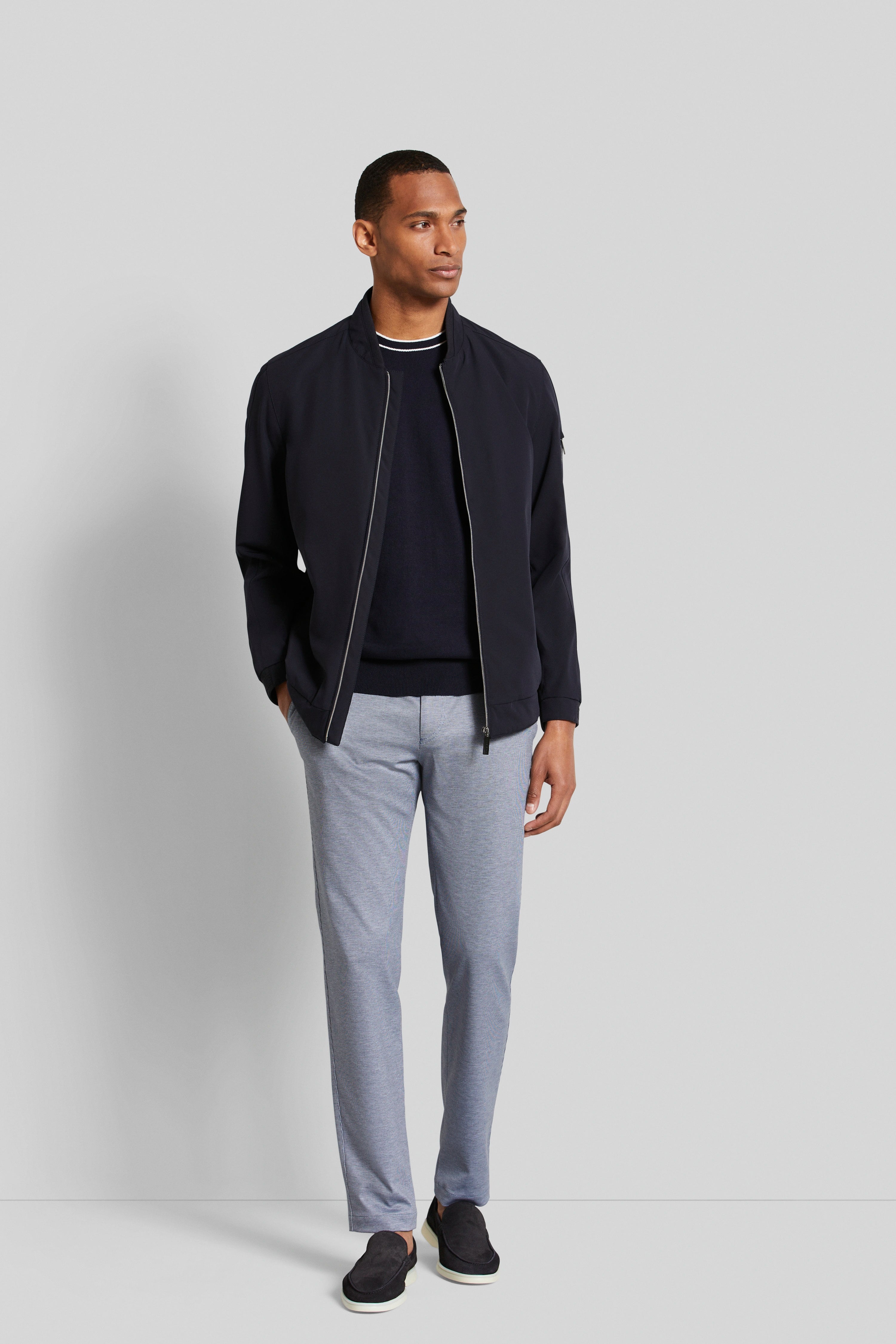 Model trägt bugatti: Dunkle Jacke, Pullover, gestreifte Hose. Lockeres Posing, Hände in Taschen.
