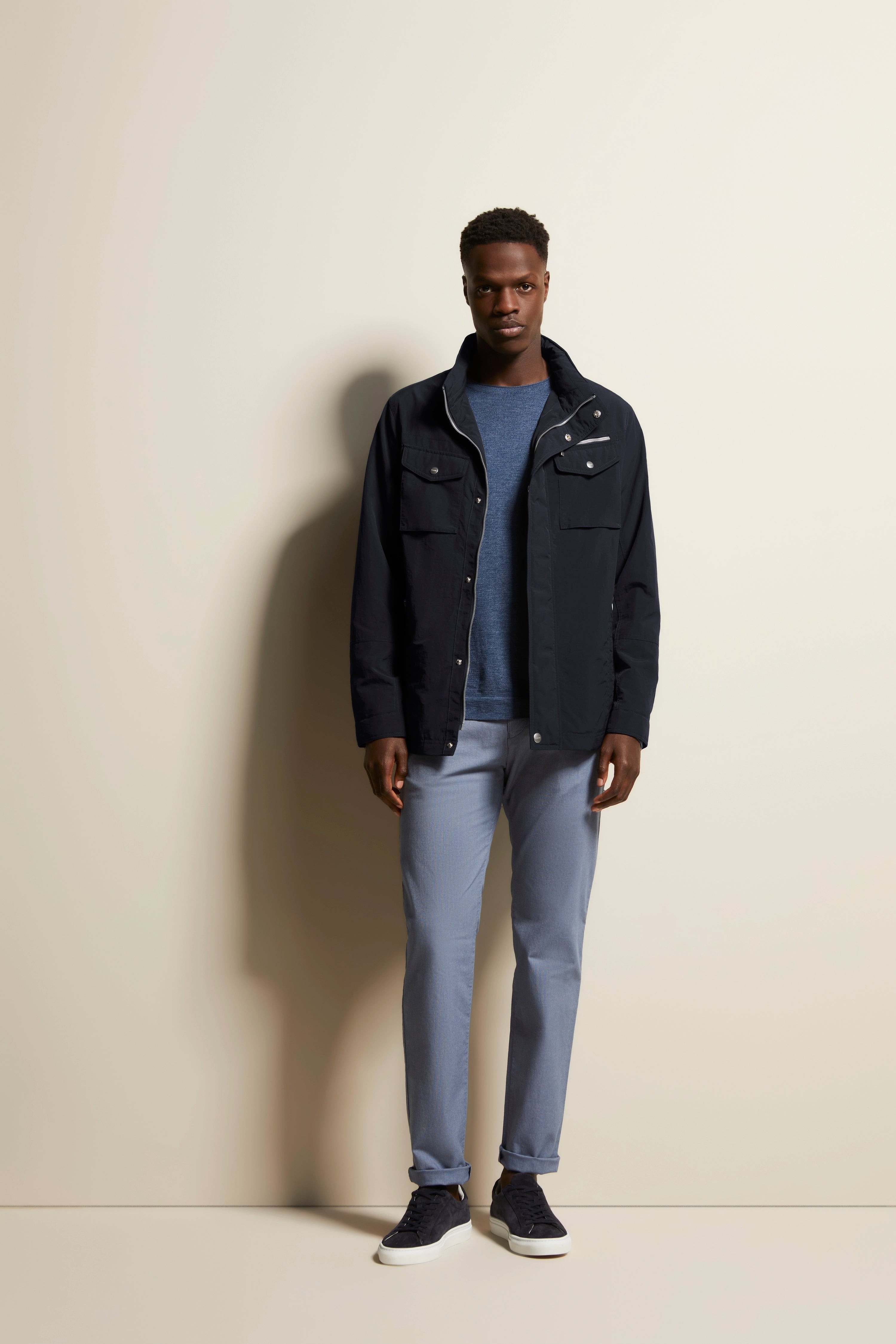Model in bugatti-Outfit: schwarze Jacke, blaues Shirt, graue Hose, dunkelblaue Schuhe. Entspanntes Posing.
