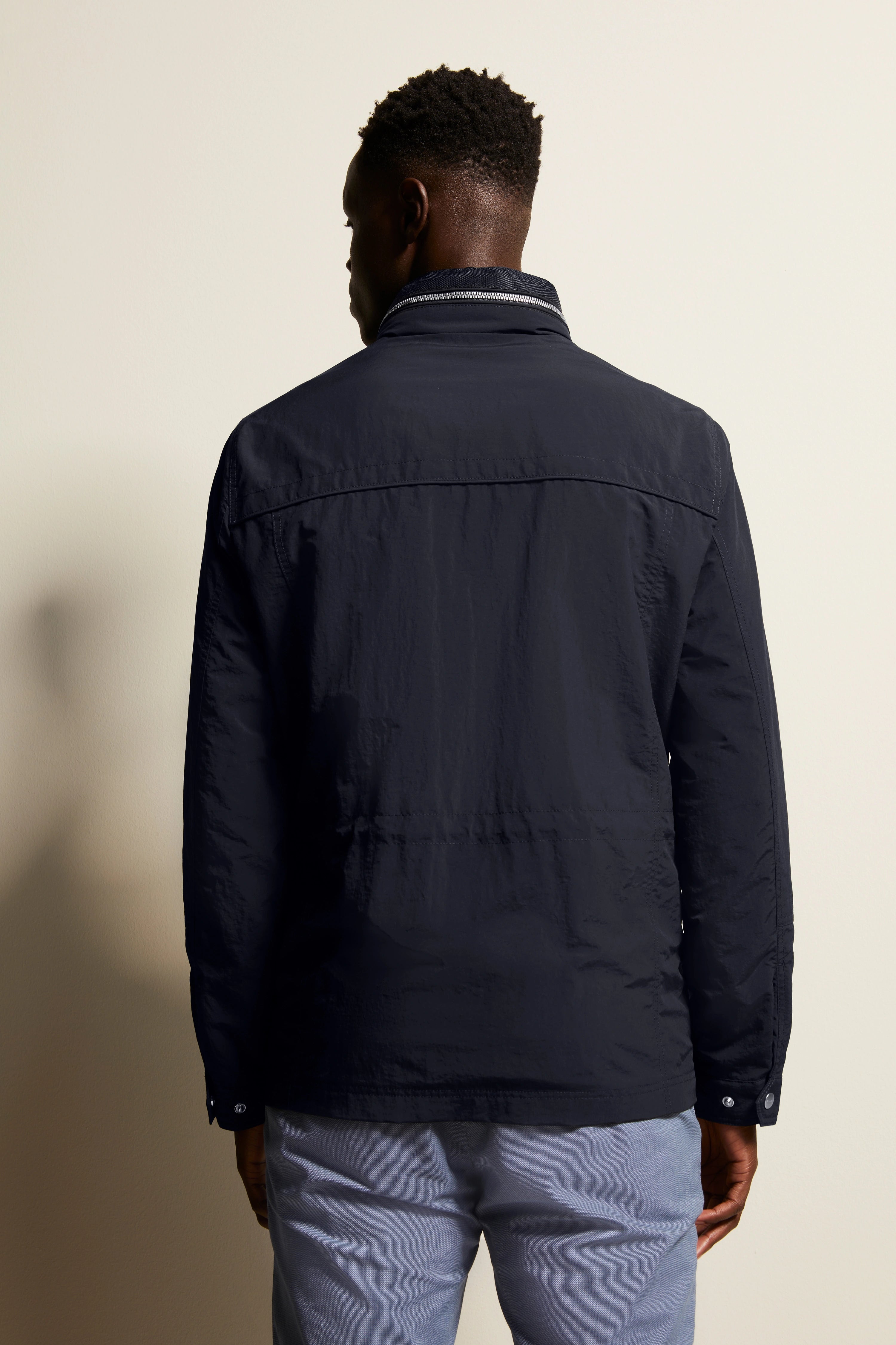 bugatti Herren Jacke in Dunkelblau, Rückansicht, mit legerem Posing, kombiniert mit hellen Hosen.