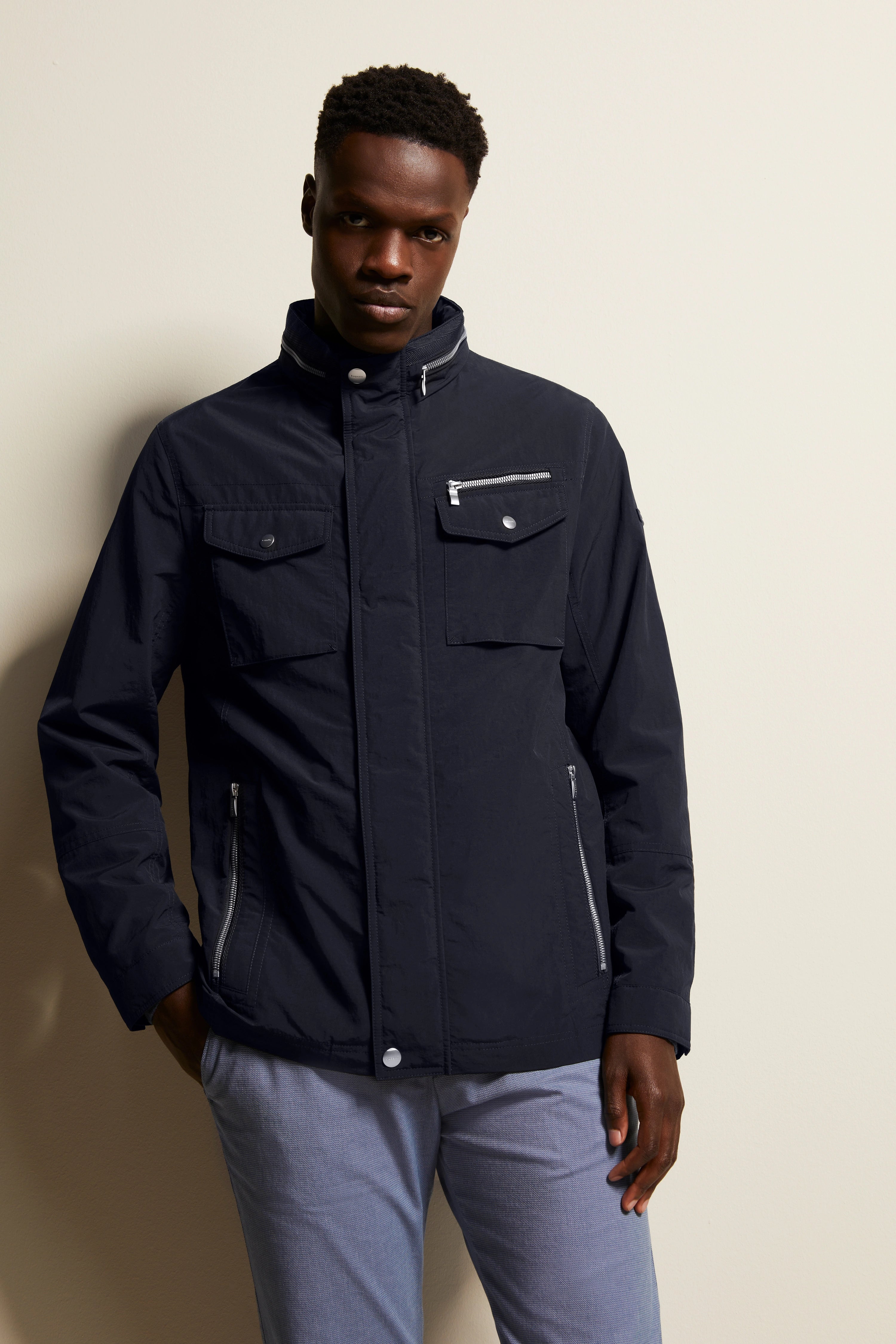 Model trägt schwarze bugatti Jacke, stehend, mit Reißverschlusstaschen, kombiniert mit hellgrauer Hose.