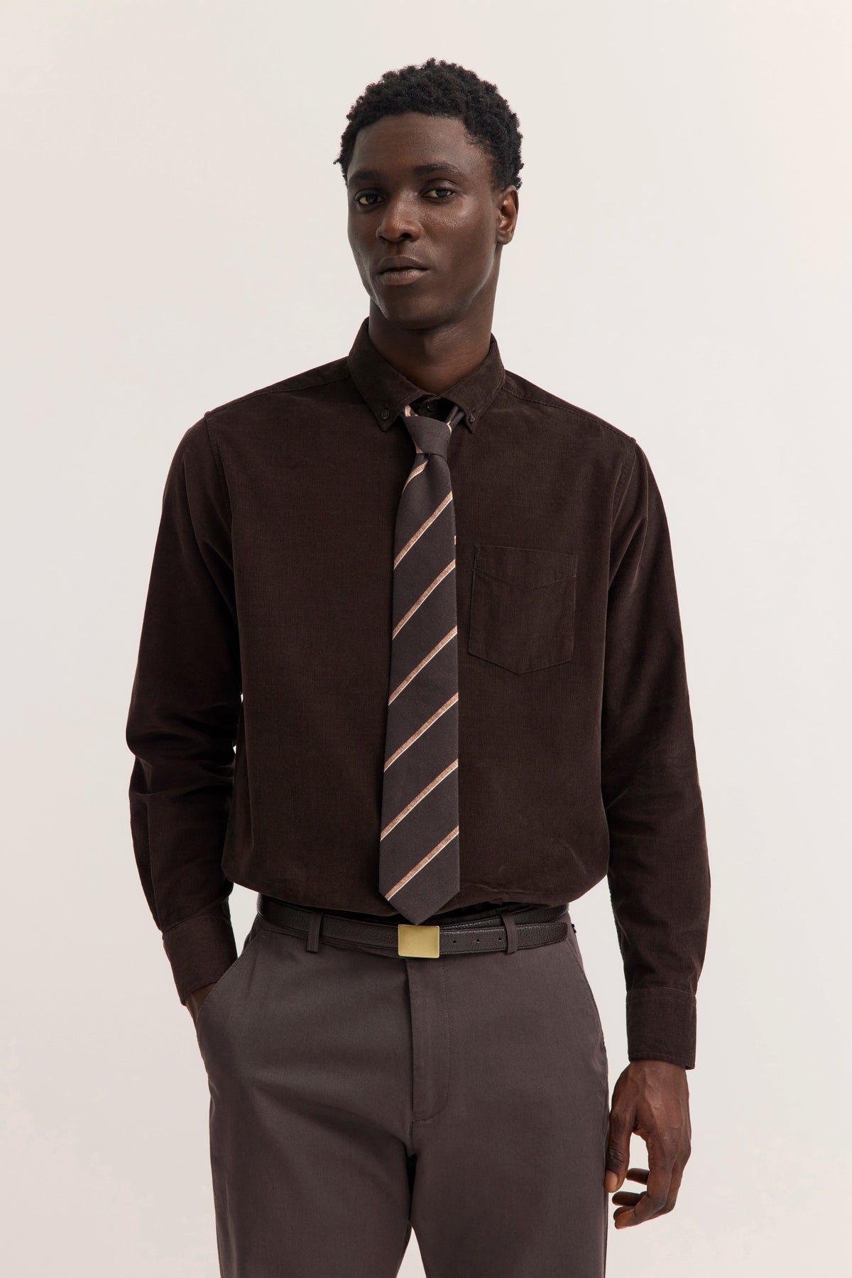 Dunkelbraunes Hemd, gestreifte Krawatte, Model steht entspannt, bugatti Stil und Eleganz.