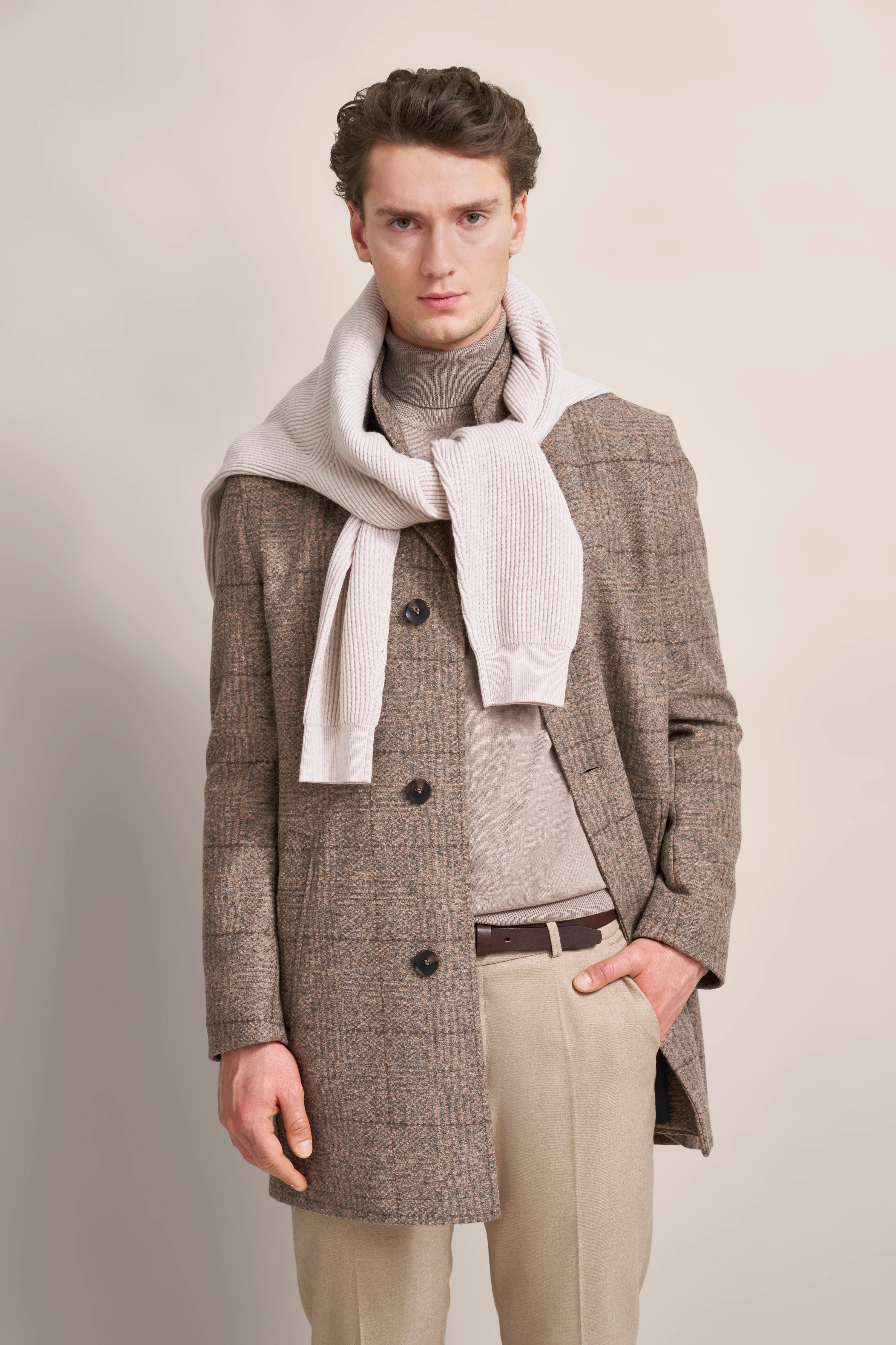 Elegantes Model in braunem karierten Mantel, beigefarbenem Rollkragen, hellem Schal und beigen Hosen.