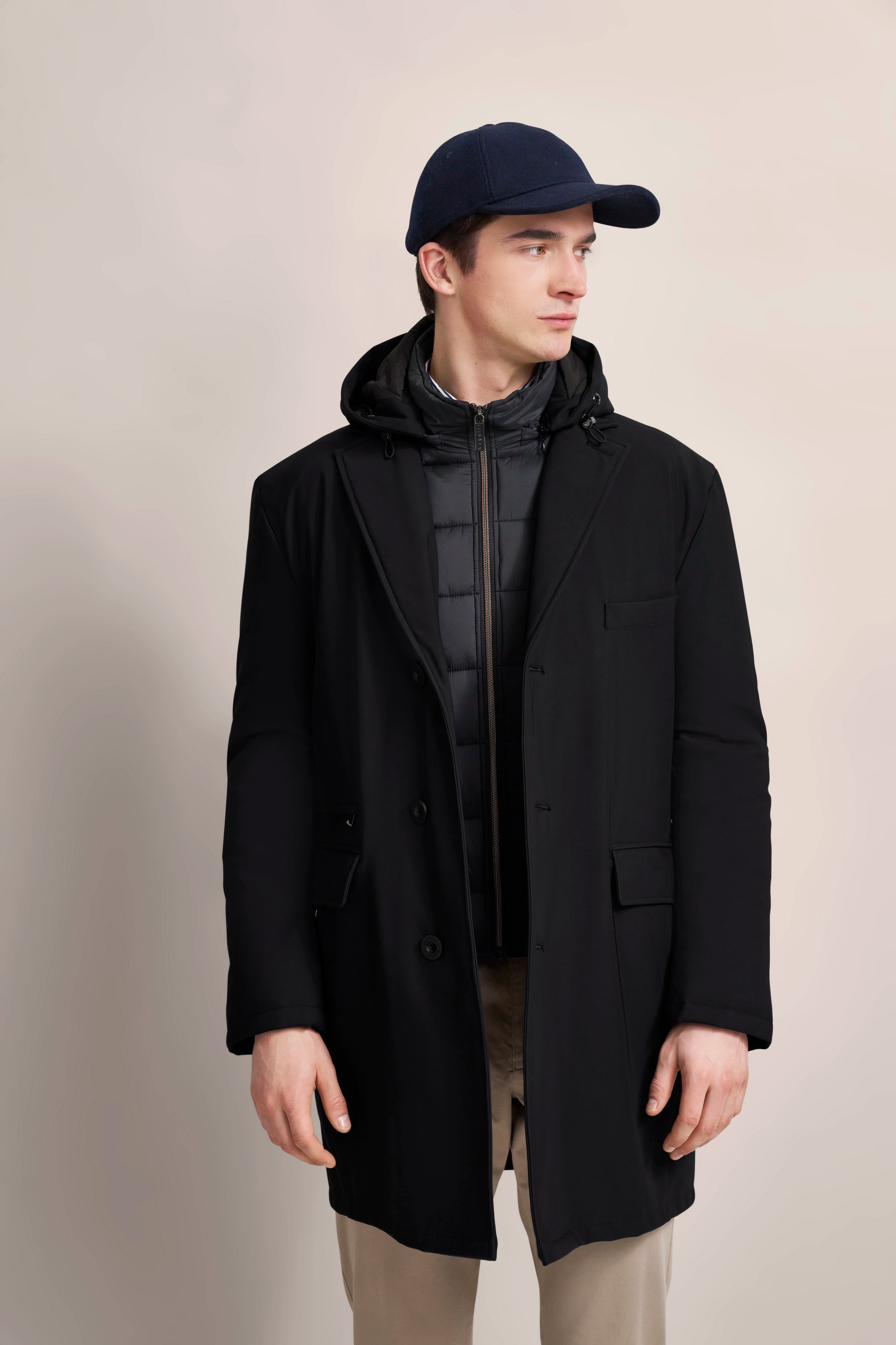 Schwarzer bugatti Mantel, dunkelblaue Kappe, Model seitlich, sportlich-elegantes Outfit.