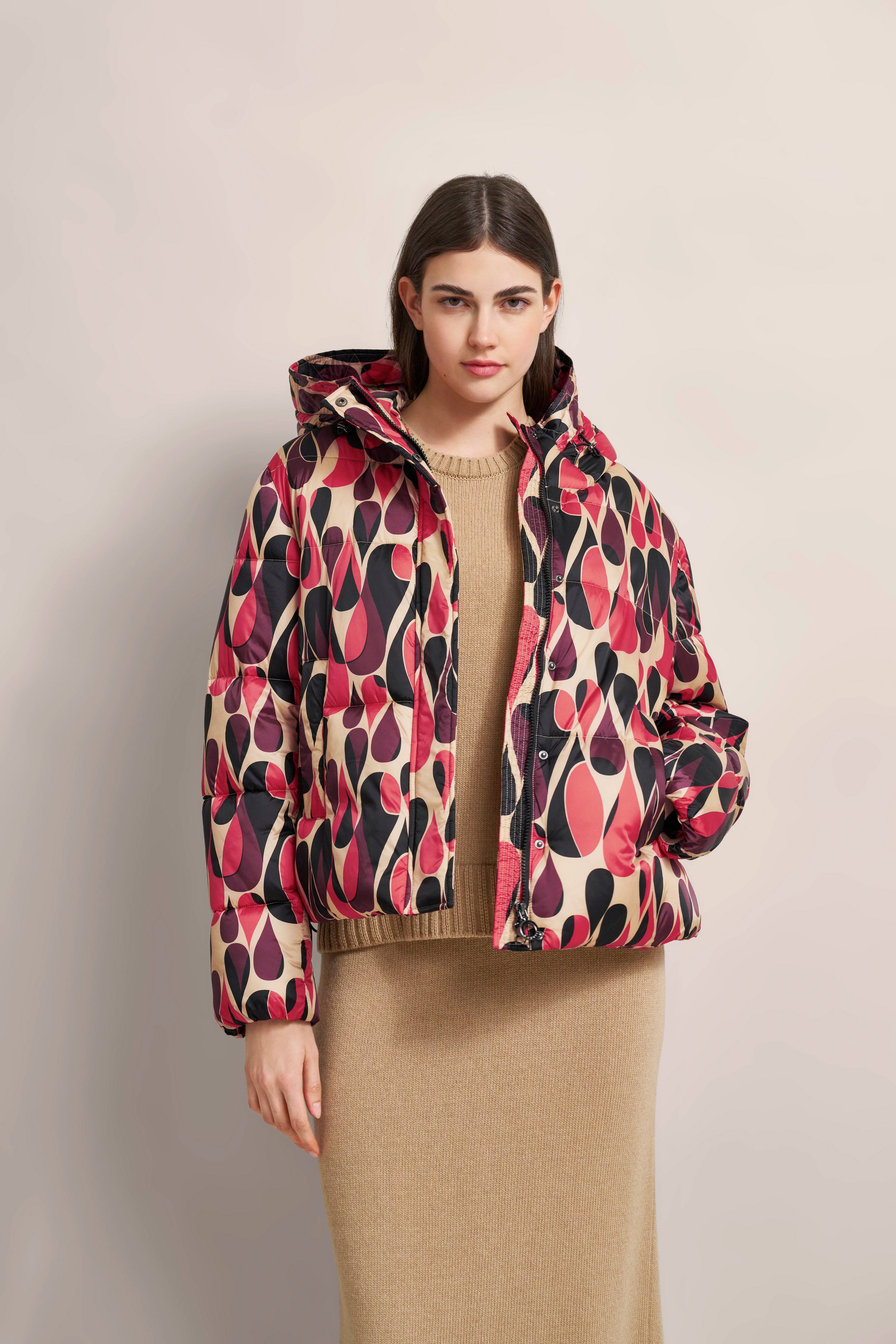 Farbige gemusterte Steppjacke und beigefarbenes Strickkleid, Modelbild, entspannte Pose.