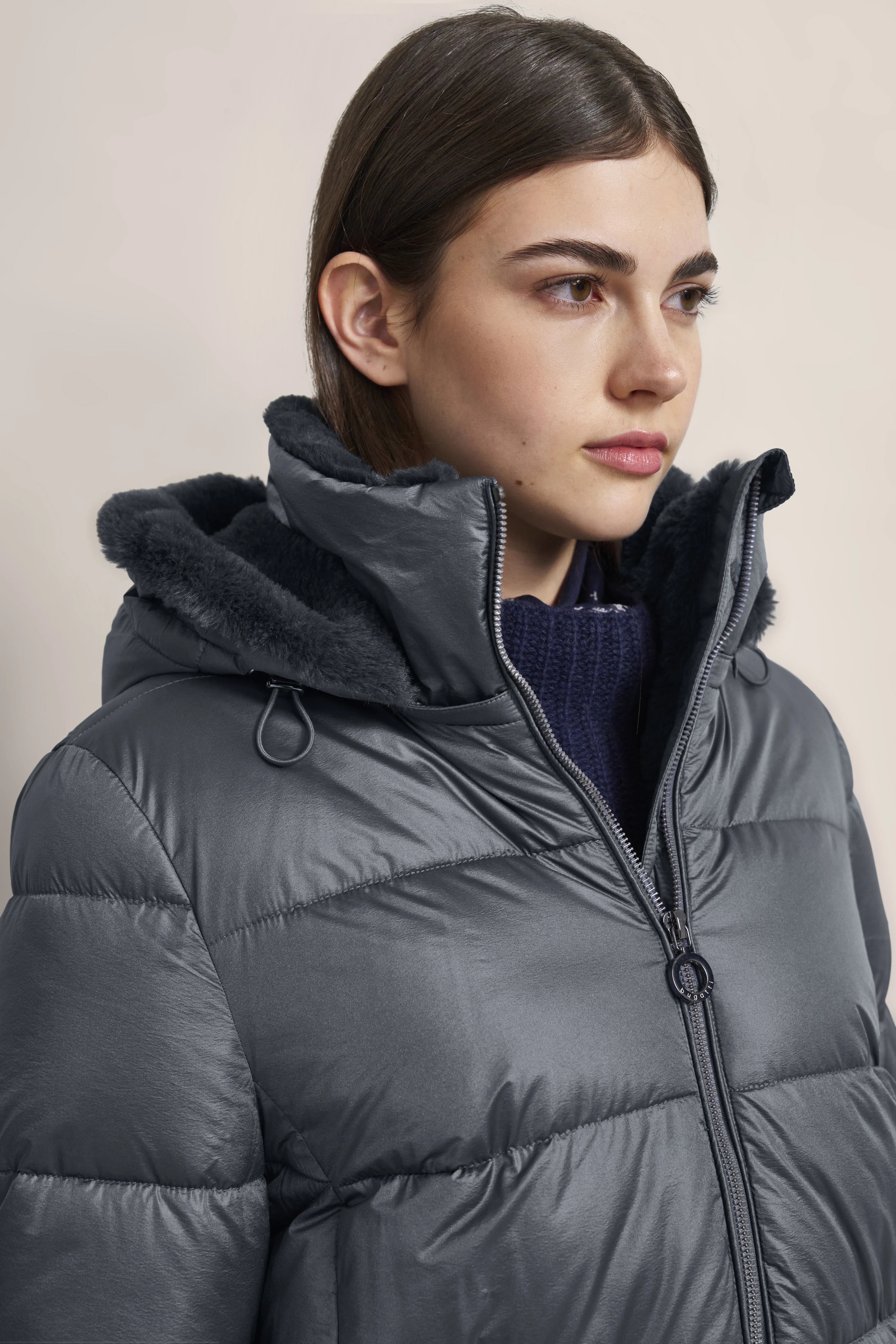 Graue Daunenjacke mit Kapuze, Model im Seitenprofil, lässig-schickes Winteroutfit von bugatti.