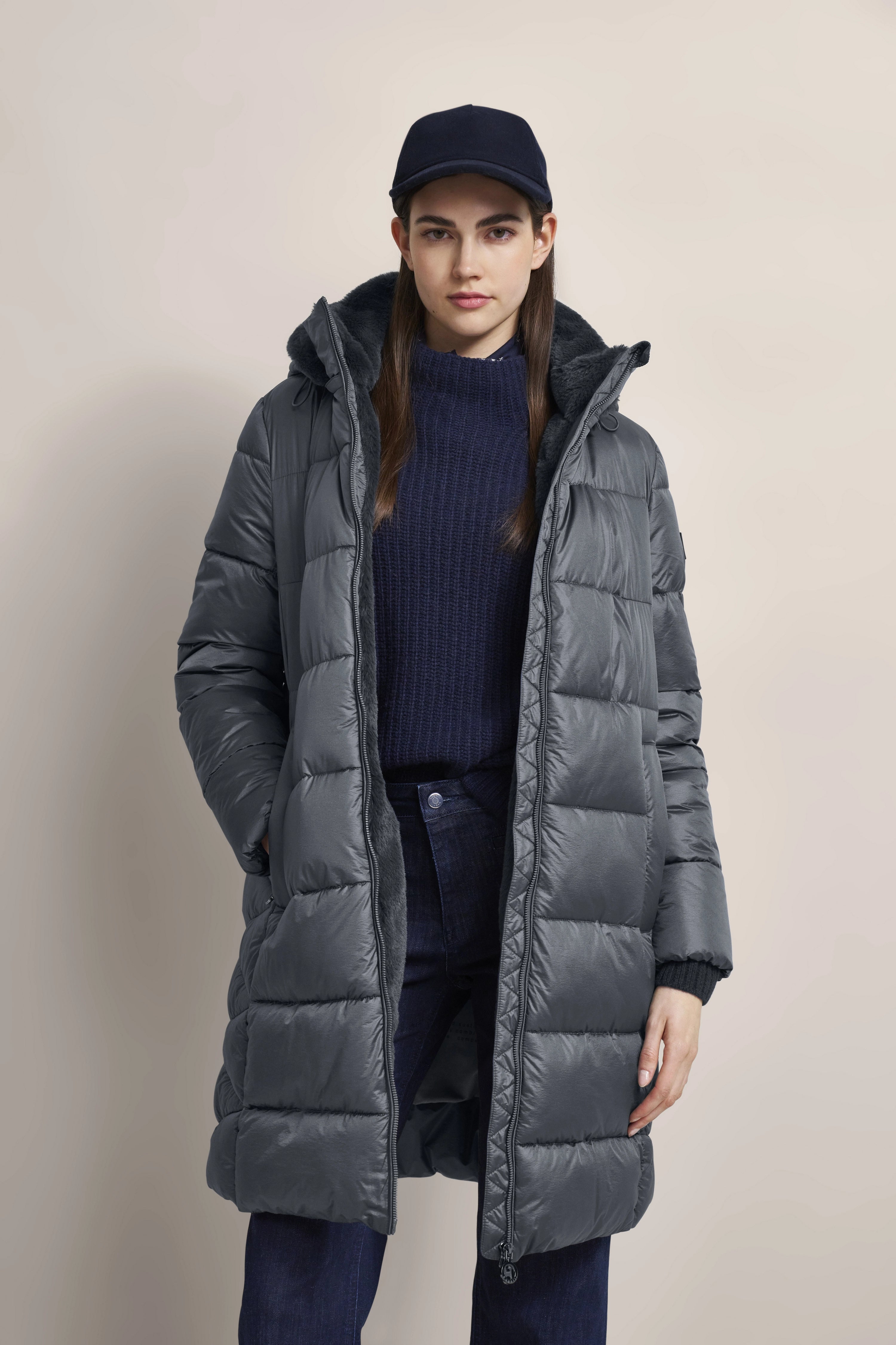 Graue Steppjacke, dunkelblauer Pullover und Mütze, lässiges Modelbild, entspannte Pose.