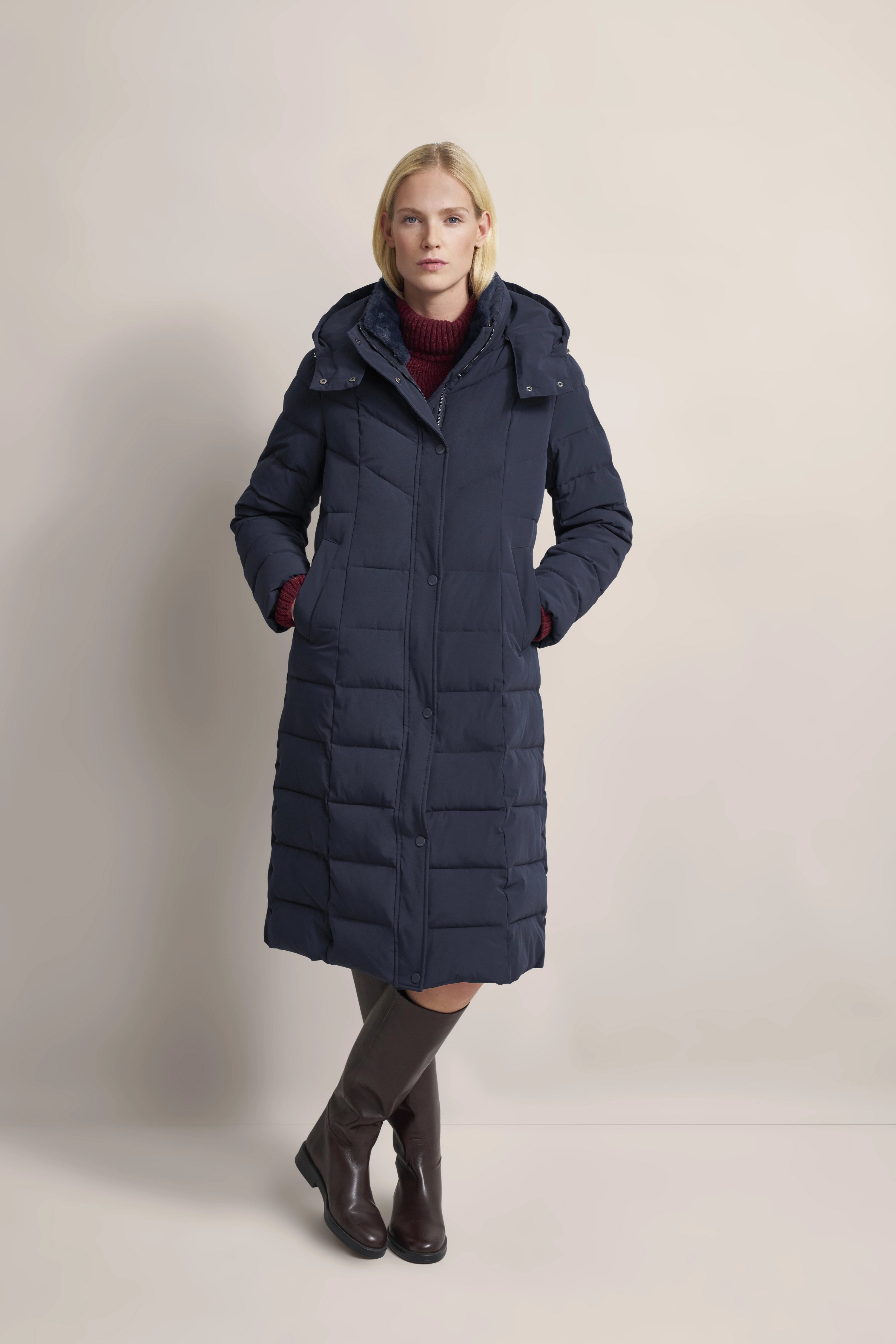 Model in navy bugatti Daunenmantel, burgunderrotem Pullover, braunen Stiefeln, entspannte Pose.