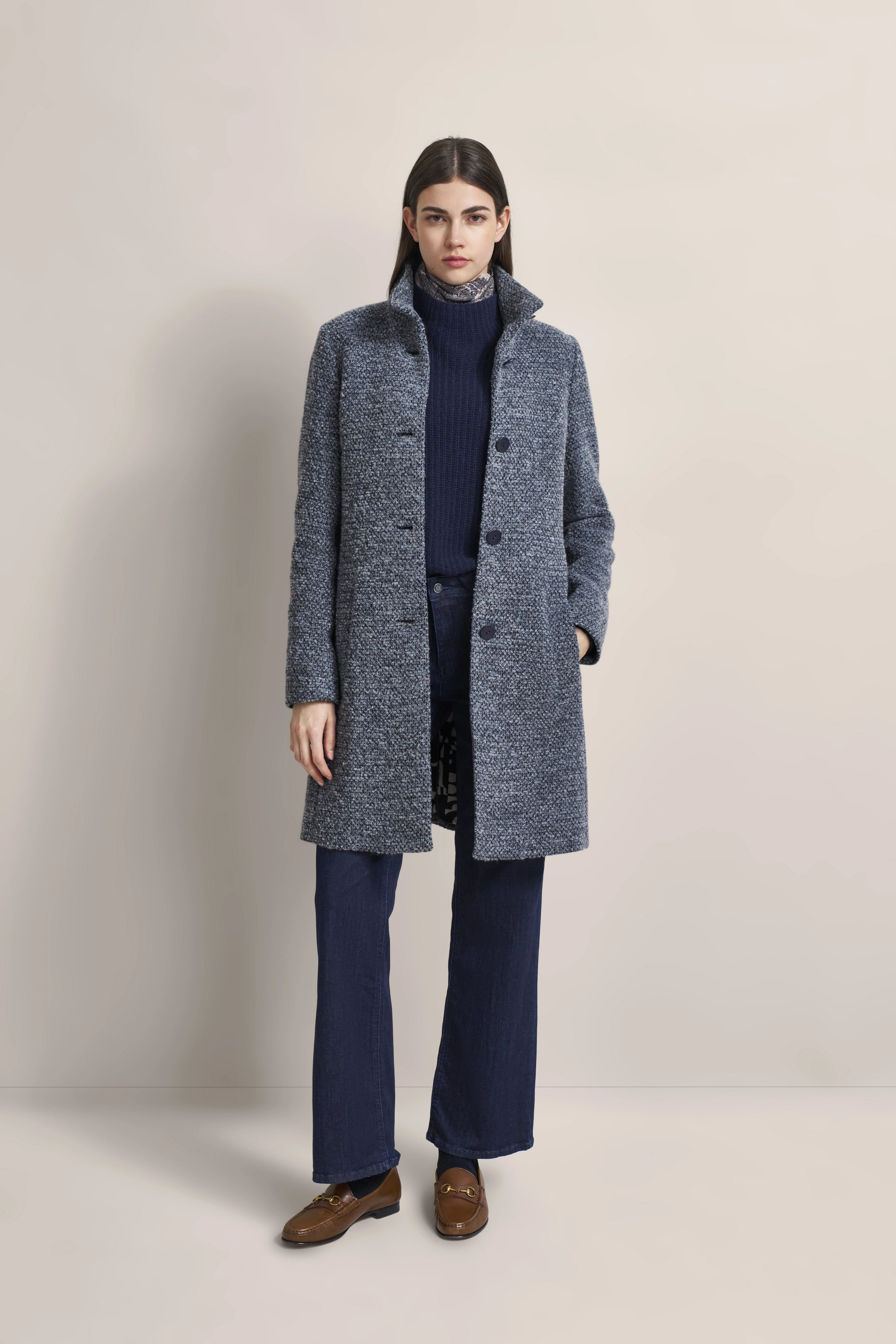 Model trägt grauen bugatti Mantel, blauen Rollkragenpullover, Jeans und braune Loafer, steht frontal.