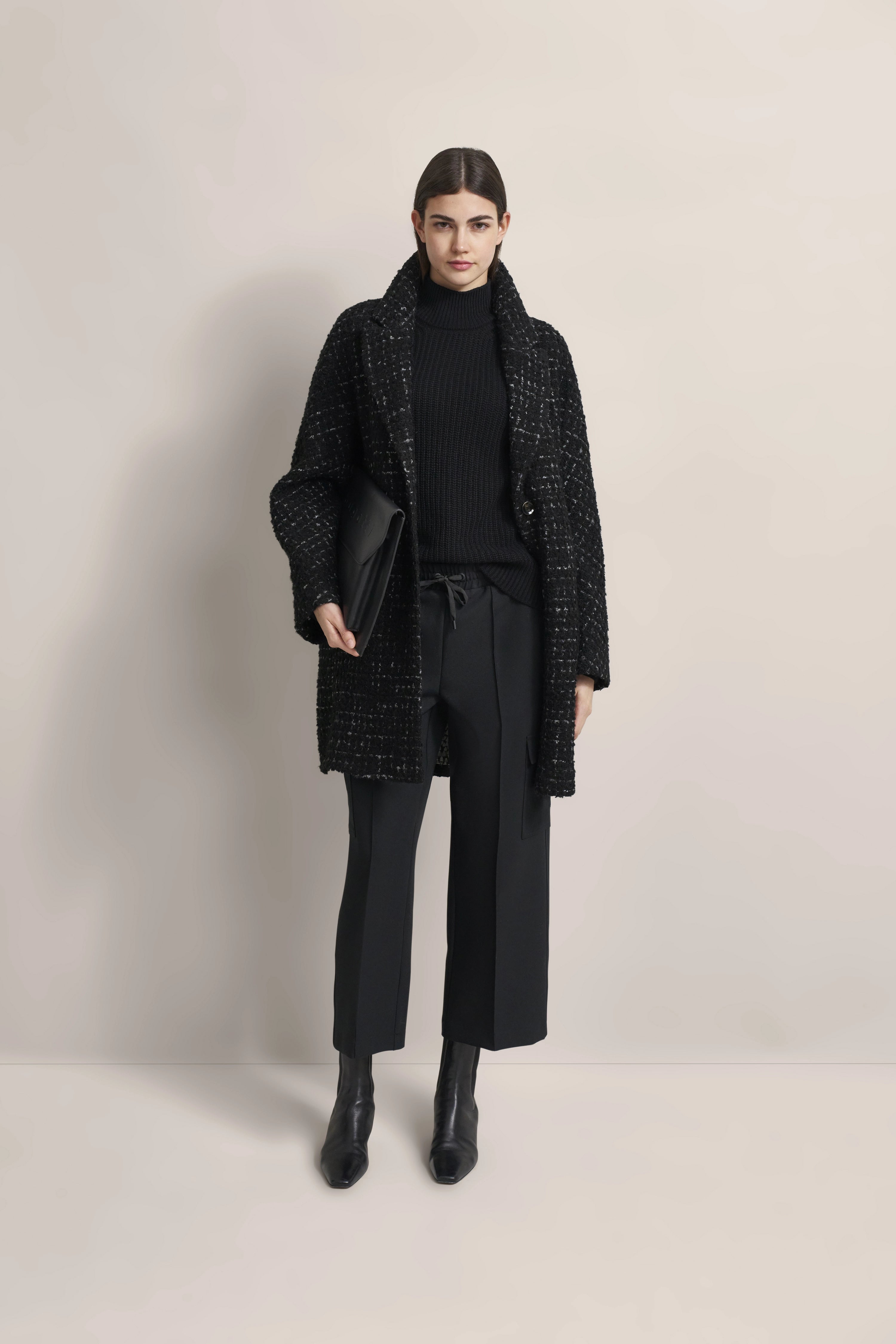 Model trägt schwarzen Mantel, Rollkragenpullover und Hose von bugatti, elegant posiert.