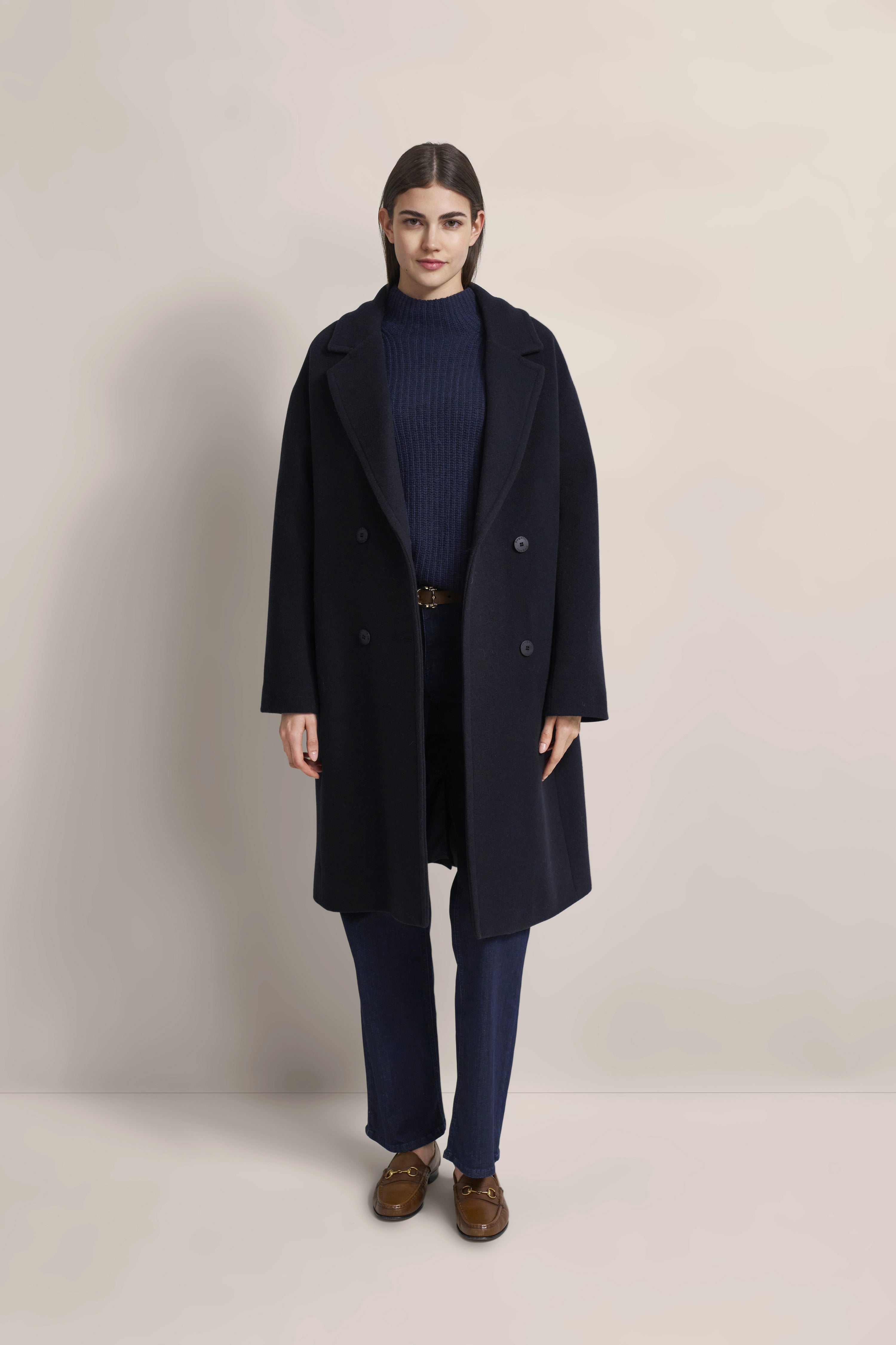 Model in navy Mantel, blauer Pullover, dunkelblaue Hose, braune Schuhe, frontal stehend.