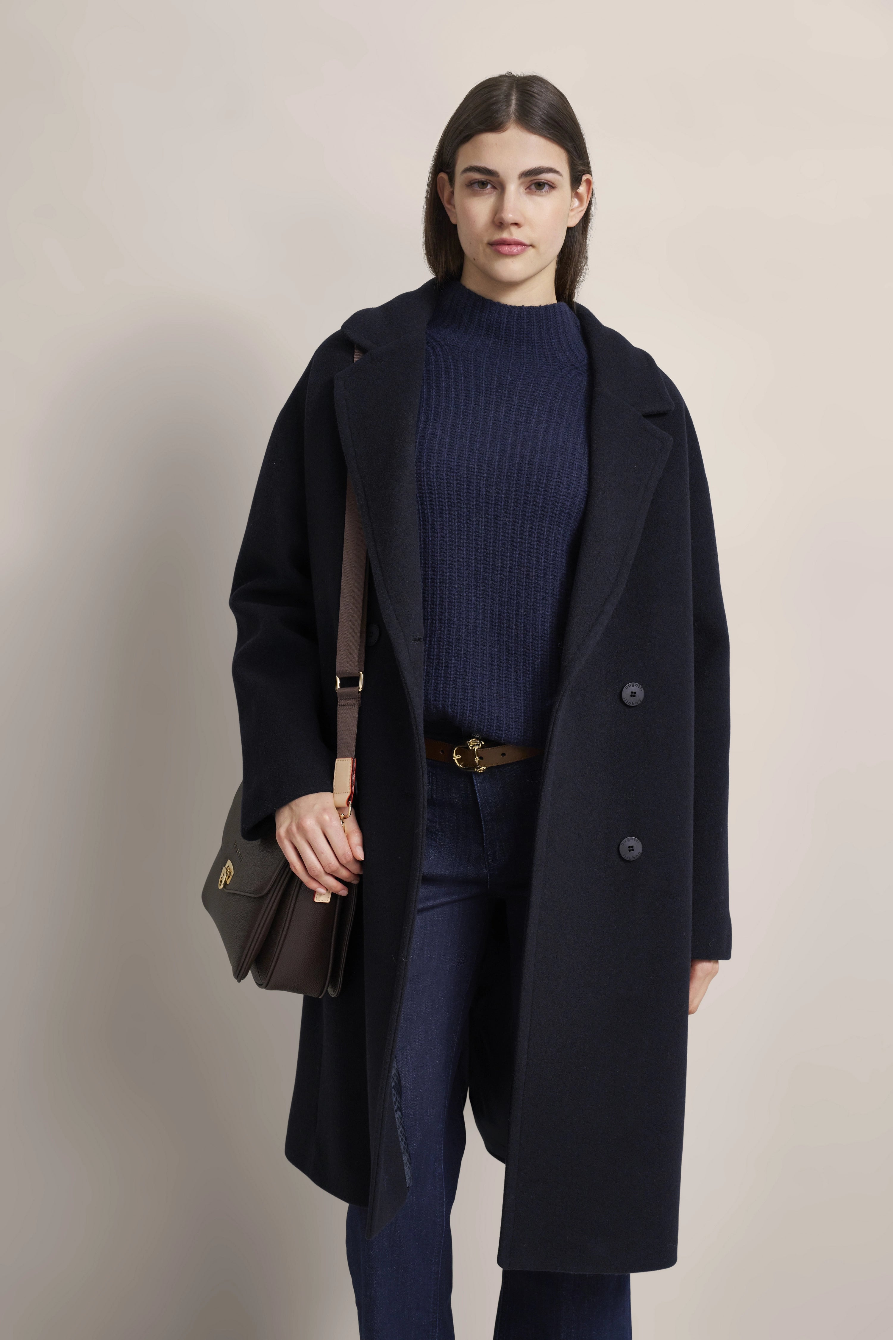 Model in dunkelblauem bugatti Mantel, navy Pullover und Jeans, legeres Posing.