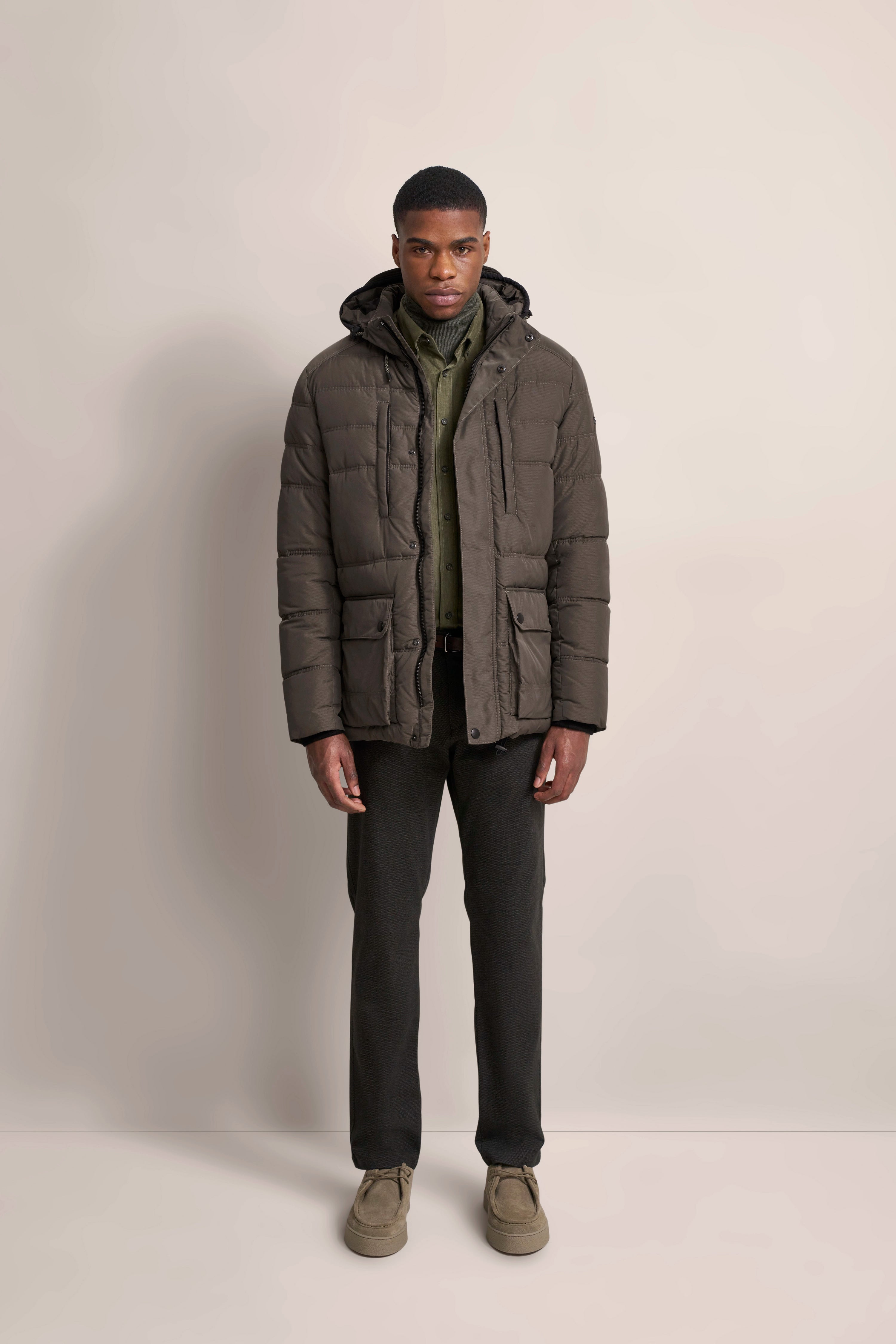 Model in olivgrüner Steppjacke, dunkelgrüner Hemd und dunklen Hosen