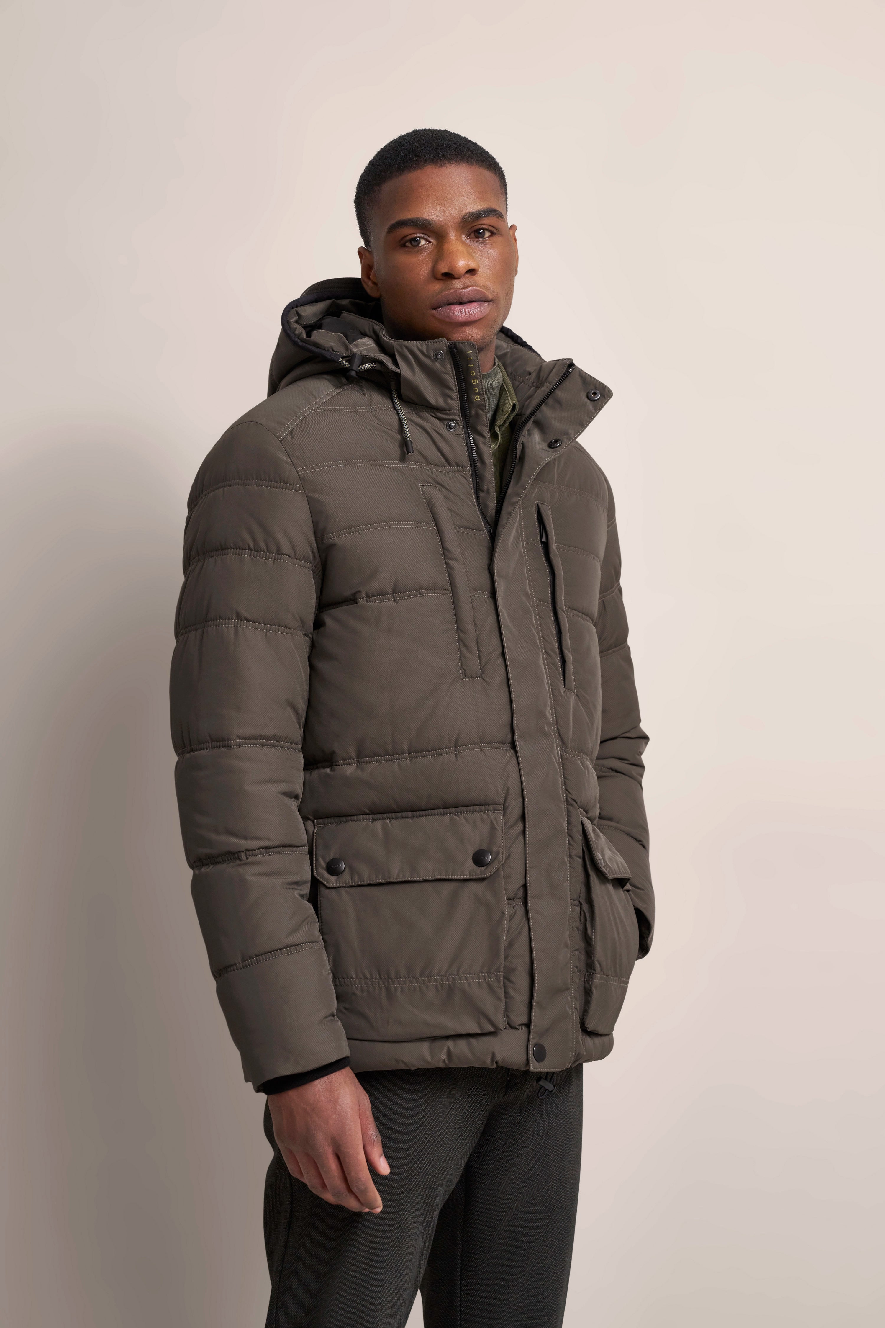 Model in olivgrüner bugatti Steppjacke, legeres Posing, Kapuze, Taschen, entspannter Look.