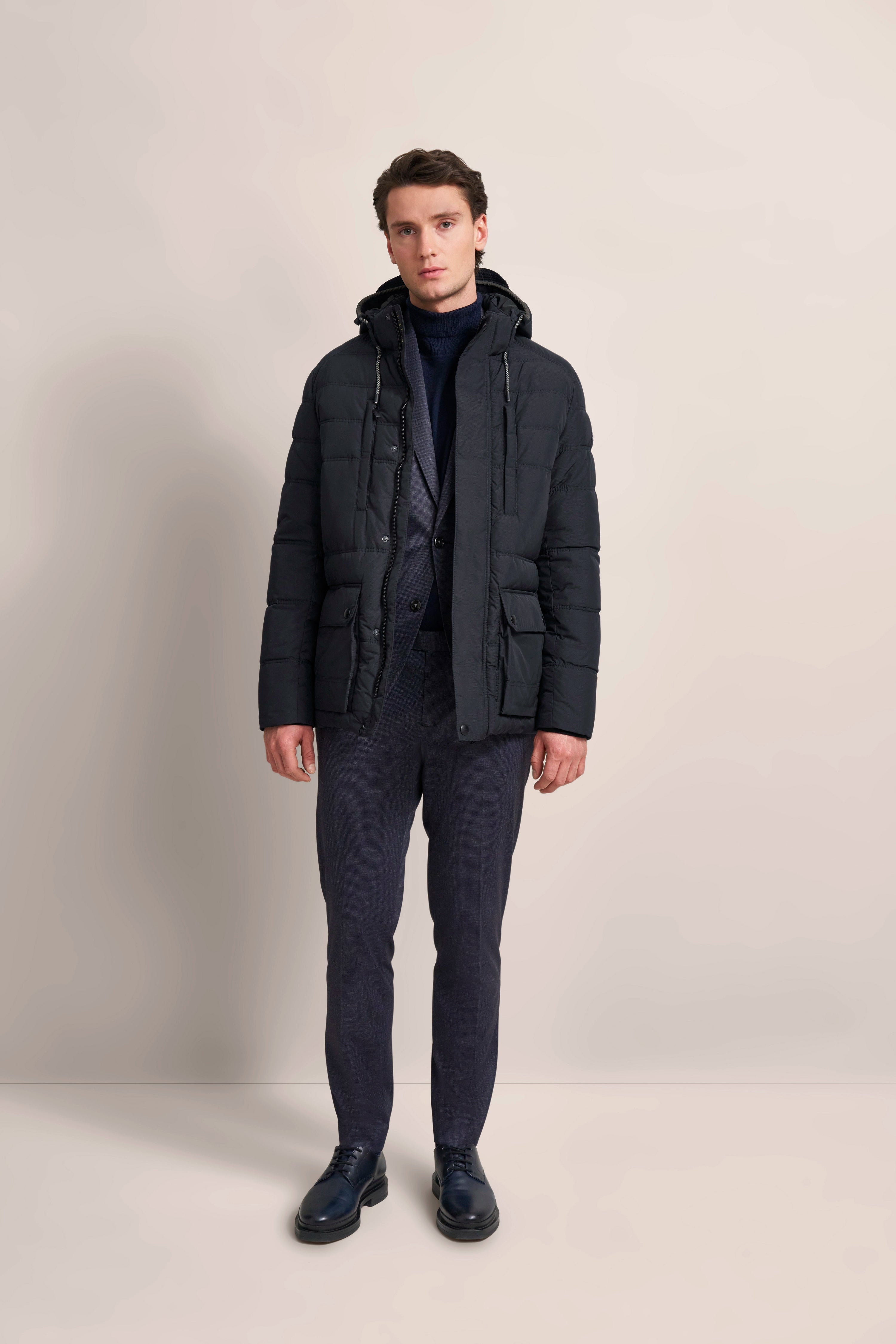 Model in schwarzer bugatti Daunenjacke, dunkelblauer Anzug und Rollkragen, gerade Haltung.