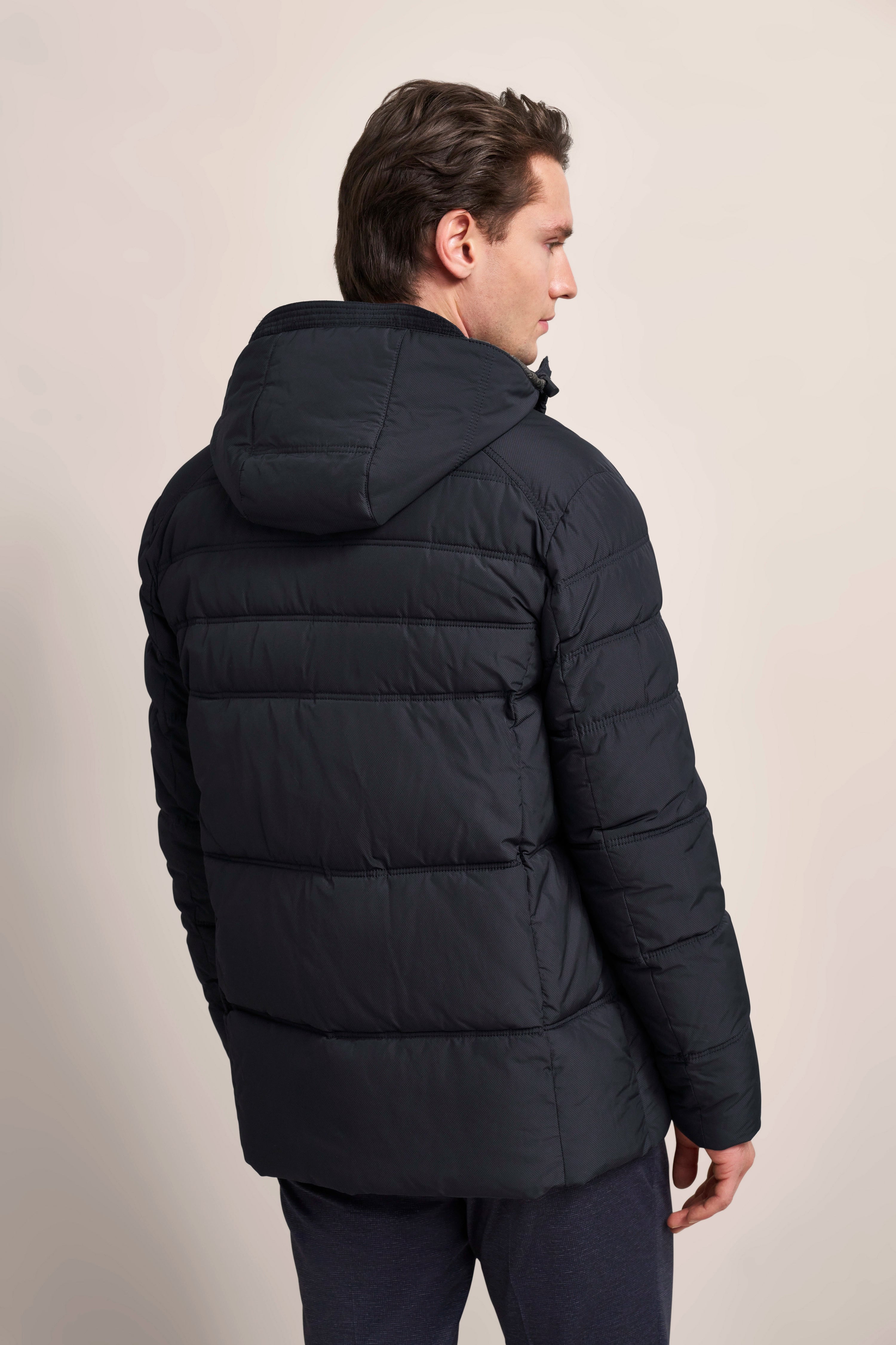 Model in schwarzer bugatti Daunenjacke, Rückansicht, legeres Posing, winterlich elegant.