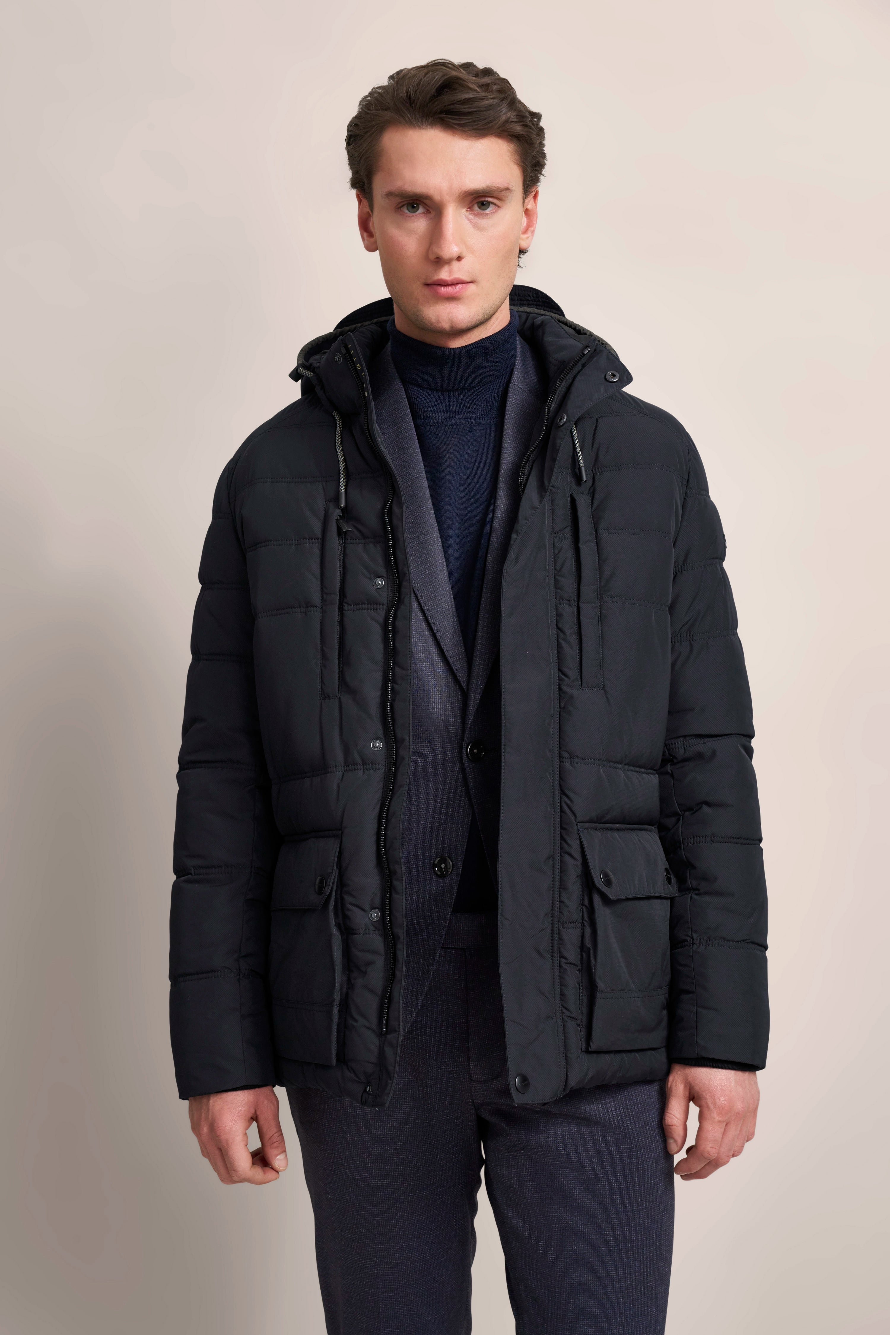 Model in schwarzer bugatti Steppjacke, dunkelblauer Anzug und Rollkragen, entspannte Haltung.